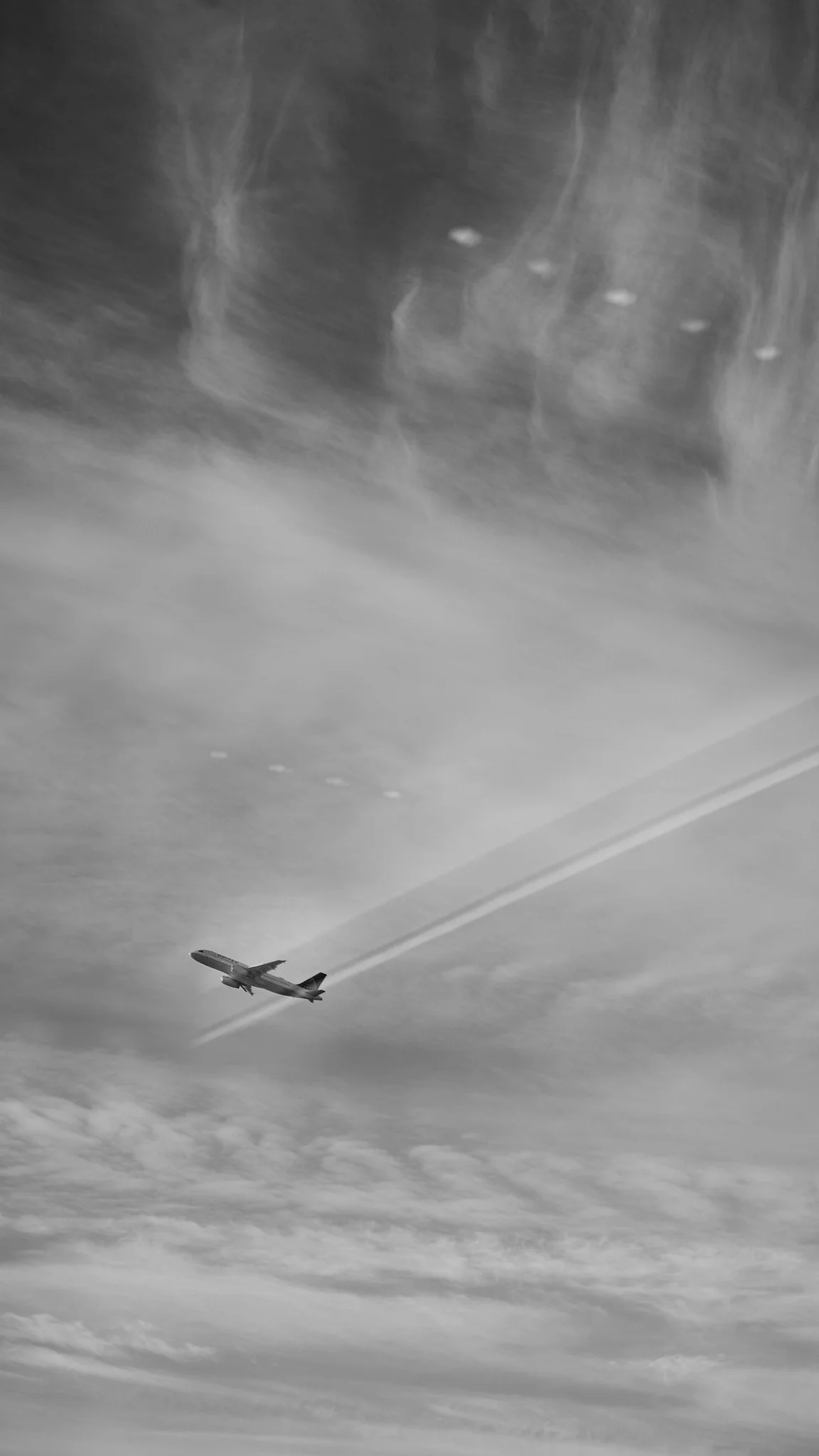 A black and white photo of an airplane in the sky, leaving a contrail behind as it flies through clouds  by Matt Ellis
