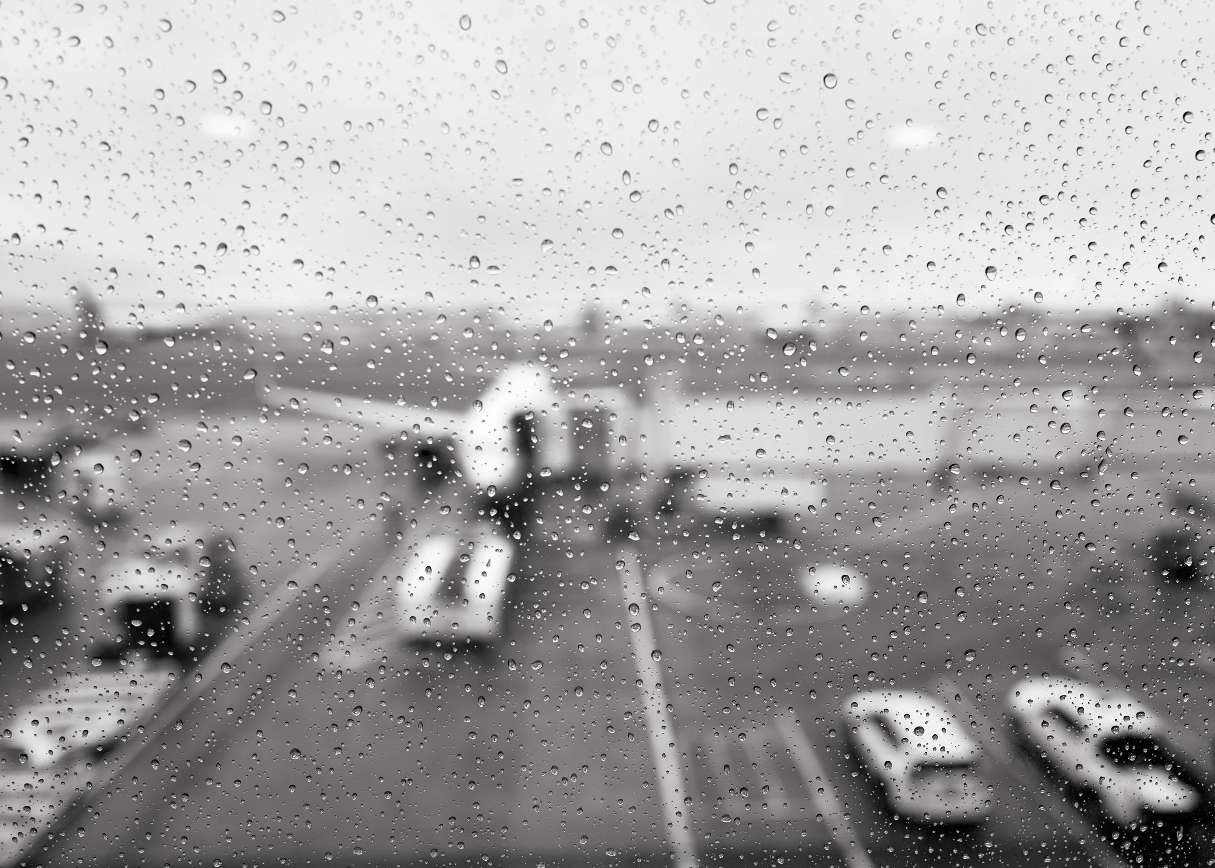 A view of an airport waiting area through a rain-covered window, with a blurred airplane on the tarmac outside.