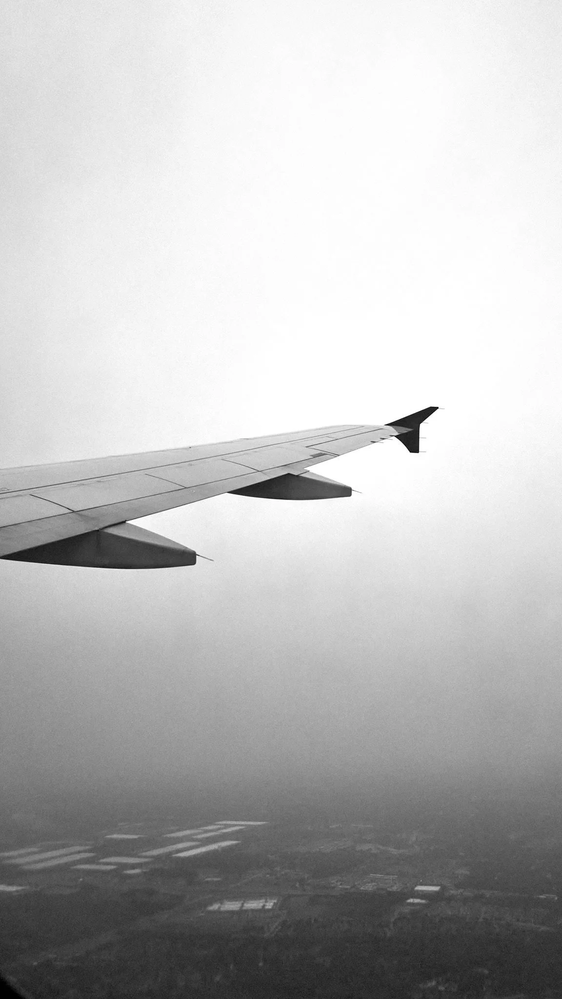View from an airplane window showing the wing of the plane and a cloudy sky with a landscape below  by Matt Ellis