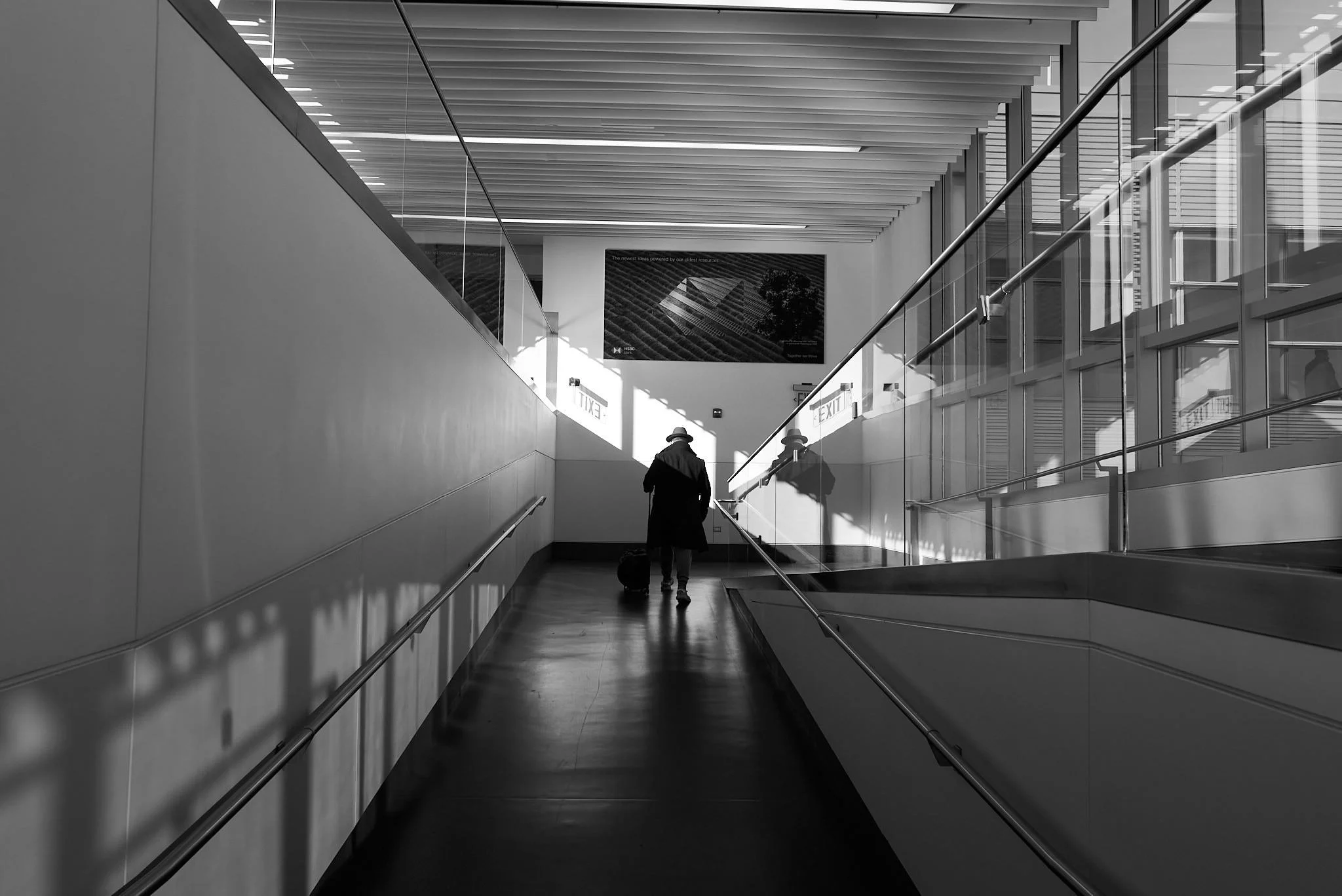 A person walking through an indoor space with modern architectural design, carrying a bag, with sunlight casting shadows on the walls.