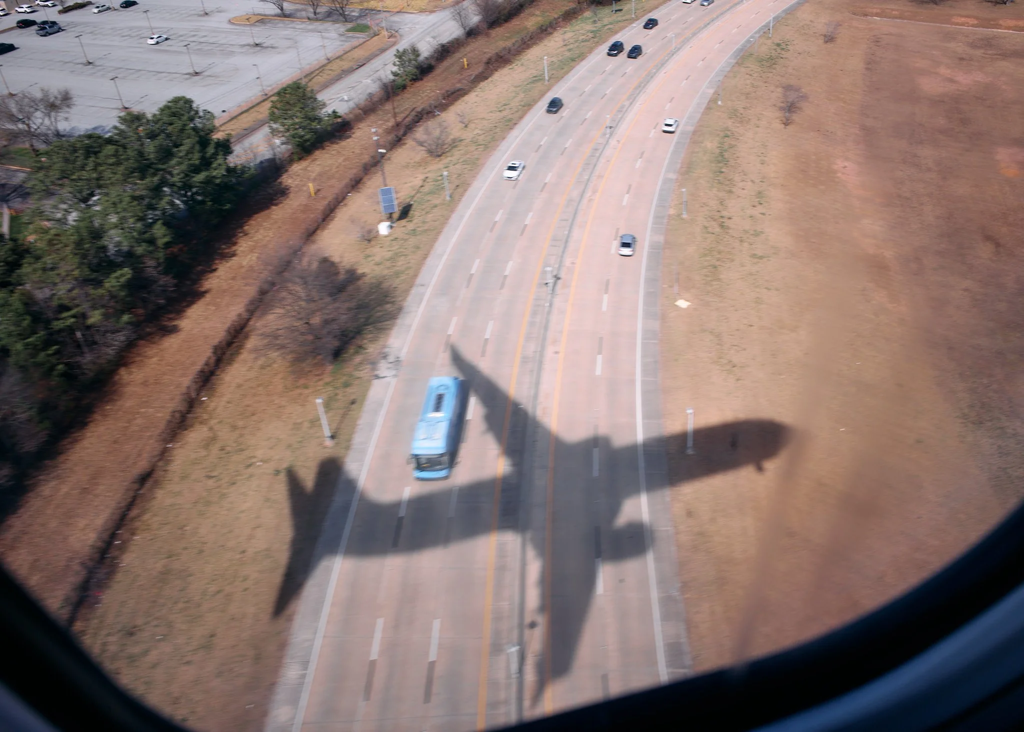 A shadow of a helicopter cast over a road with cars and a bus, aerial view from a window  by Matt Ellis