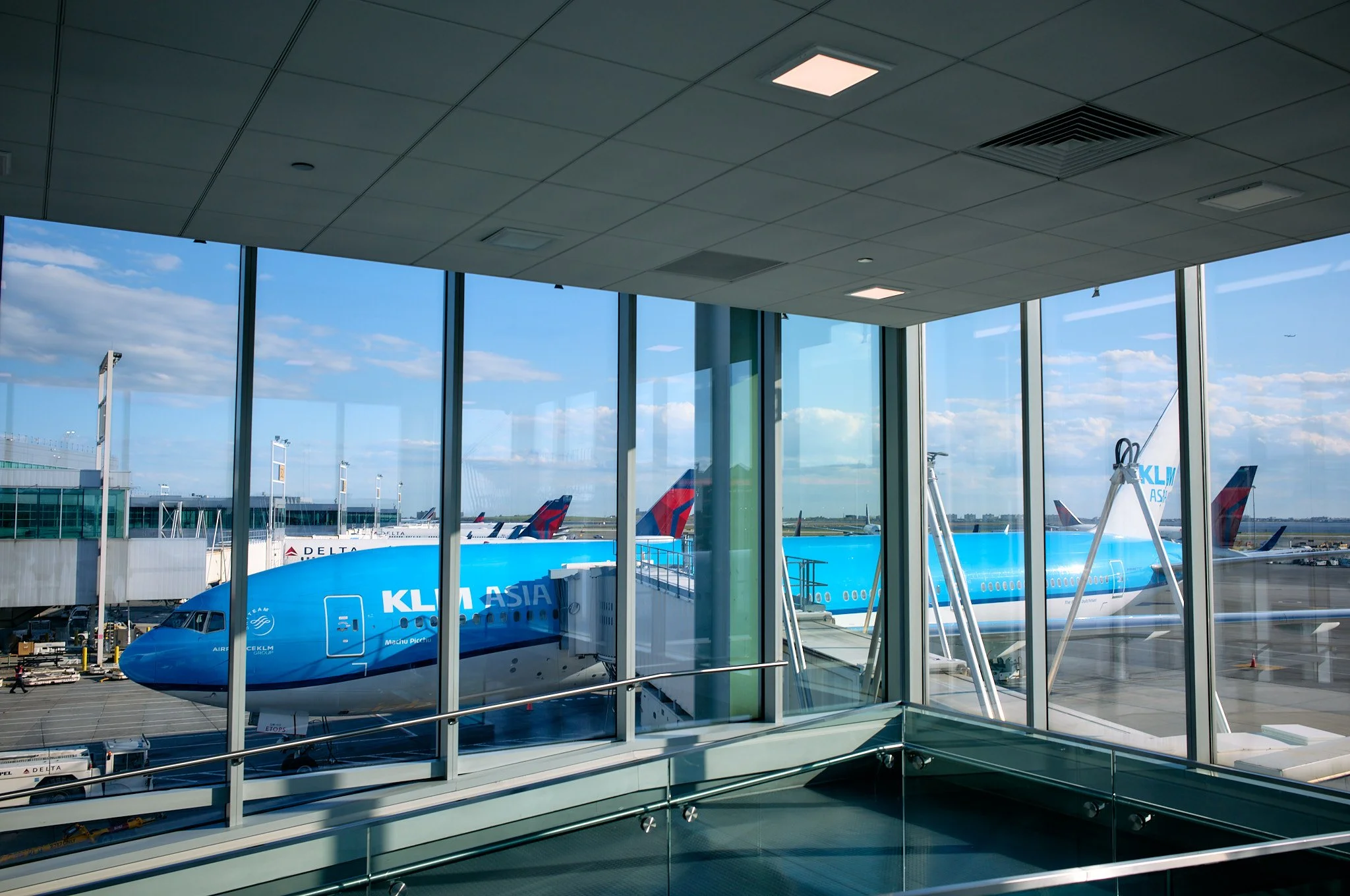 View of an airport terminal with windows showing a large blue KLM Royal Dutch Airlines airplane parked at the gate, with other airplanes visible on the tarmac outside. photo by Matt Ellis