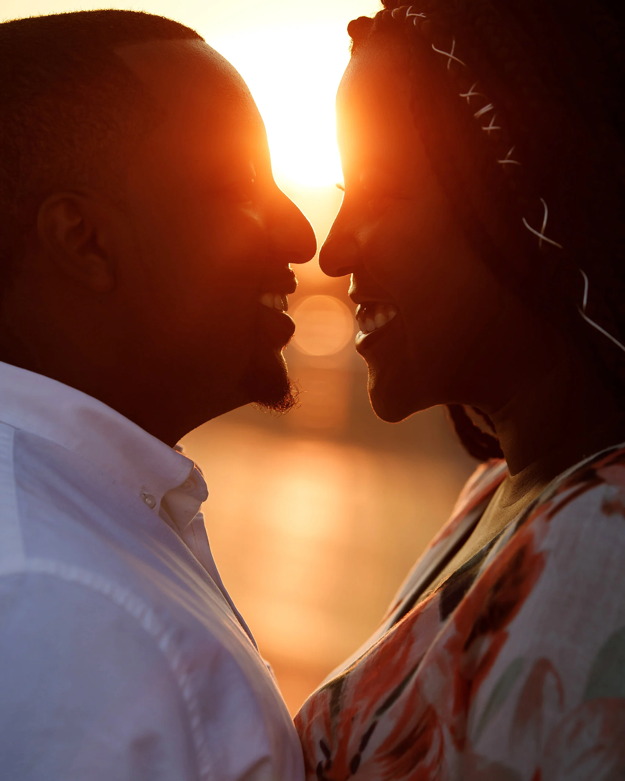 A couple facing each other close to sunset, smiling and touching foreheads.