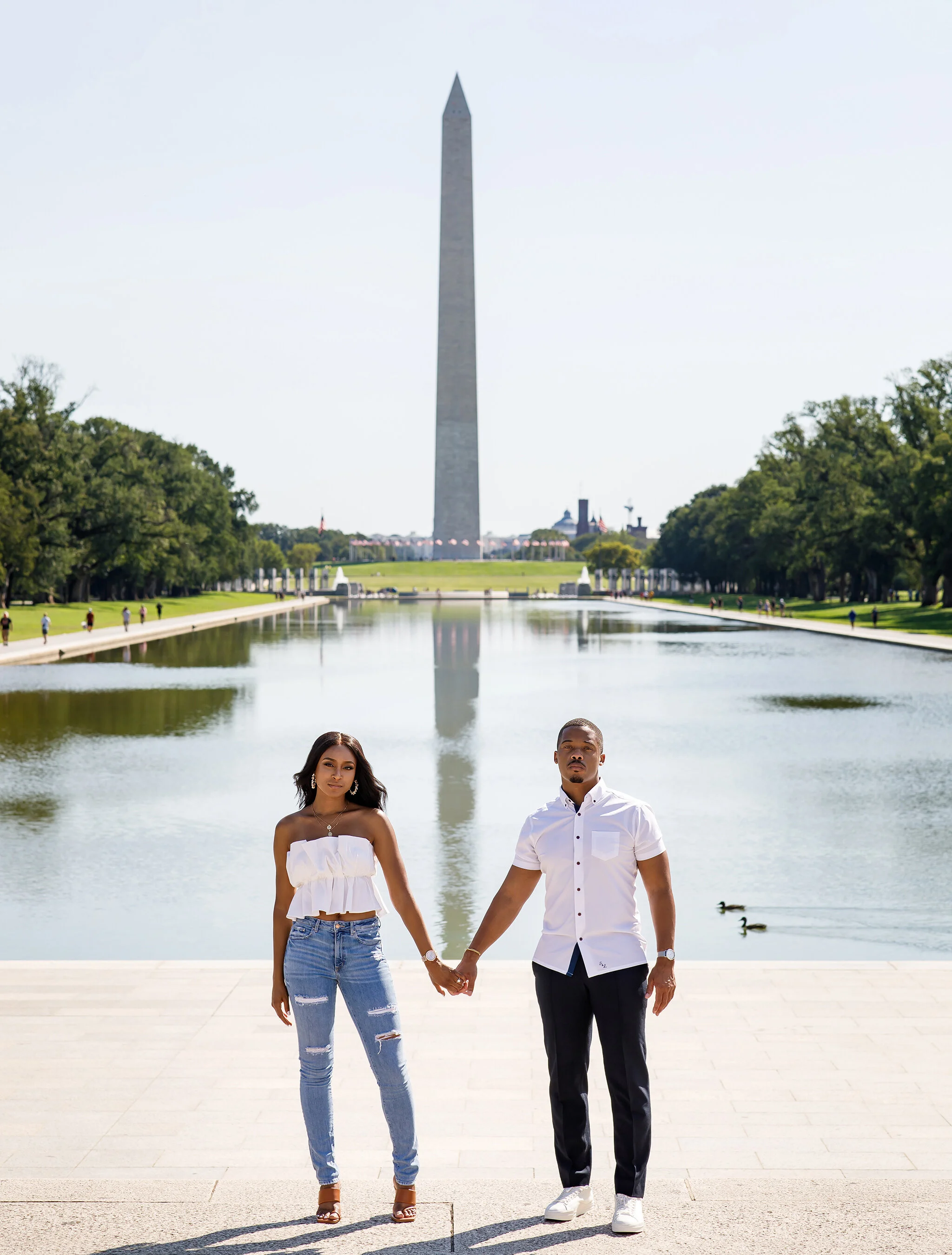 A couple holding hands standing by the Reflecting Pool with the Washington Monument in the background, in Washington, D.C.
