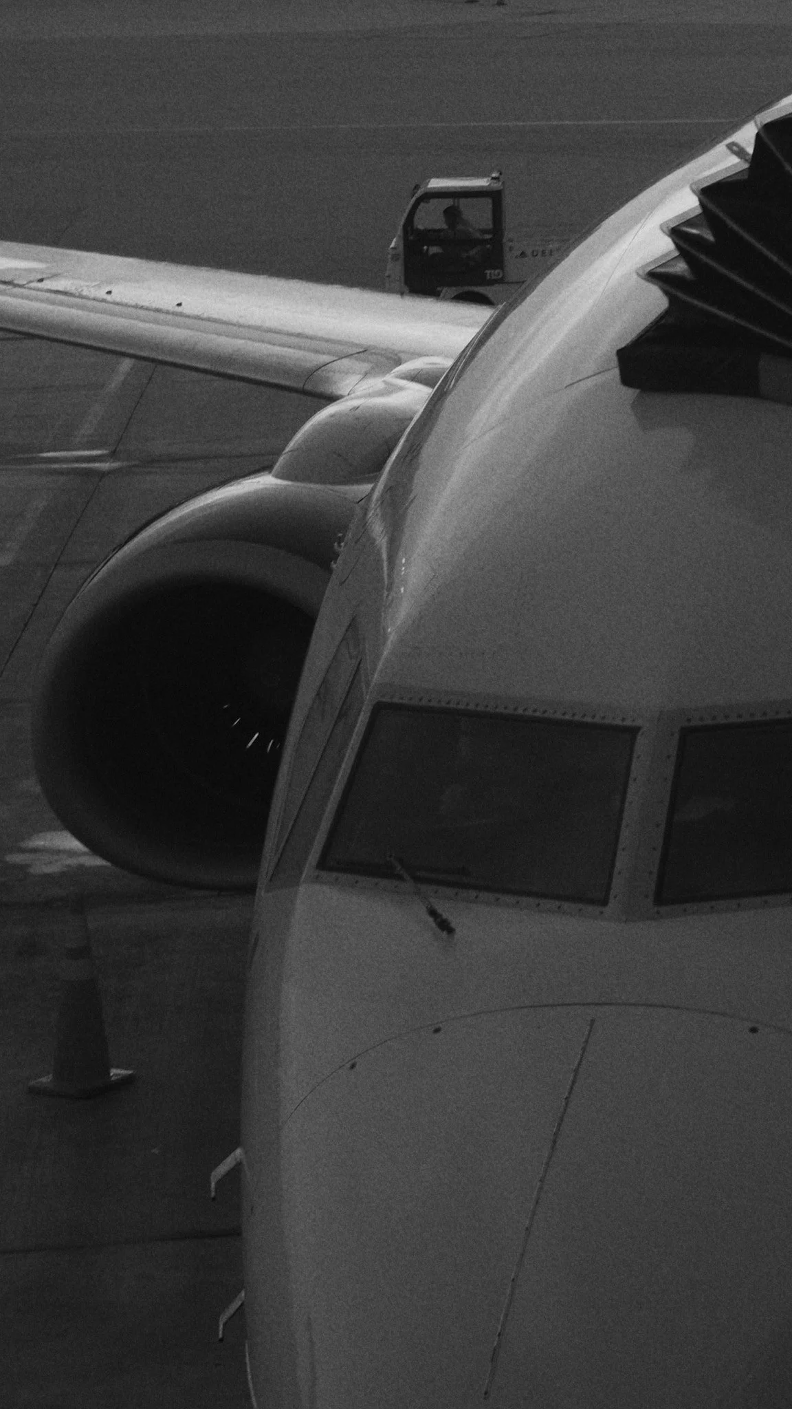 Close-up of the front section of an airplane, including the cockpit windows and part of the jet engine, with a towing vehicle in the background.