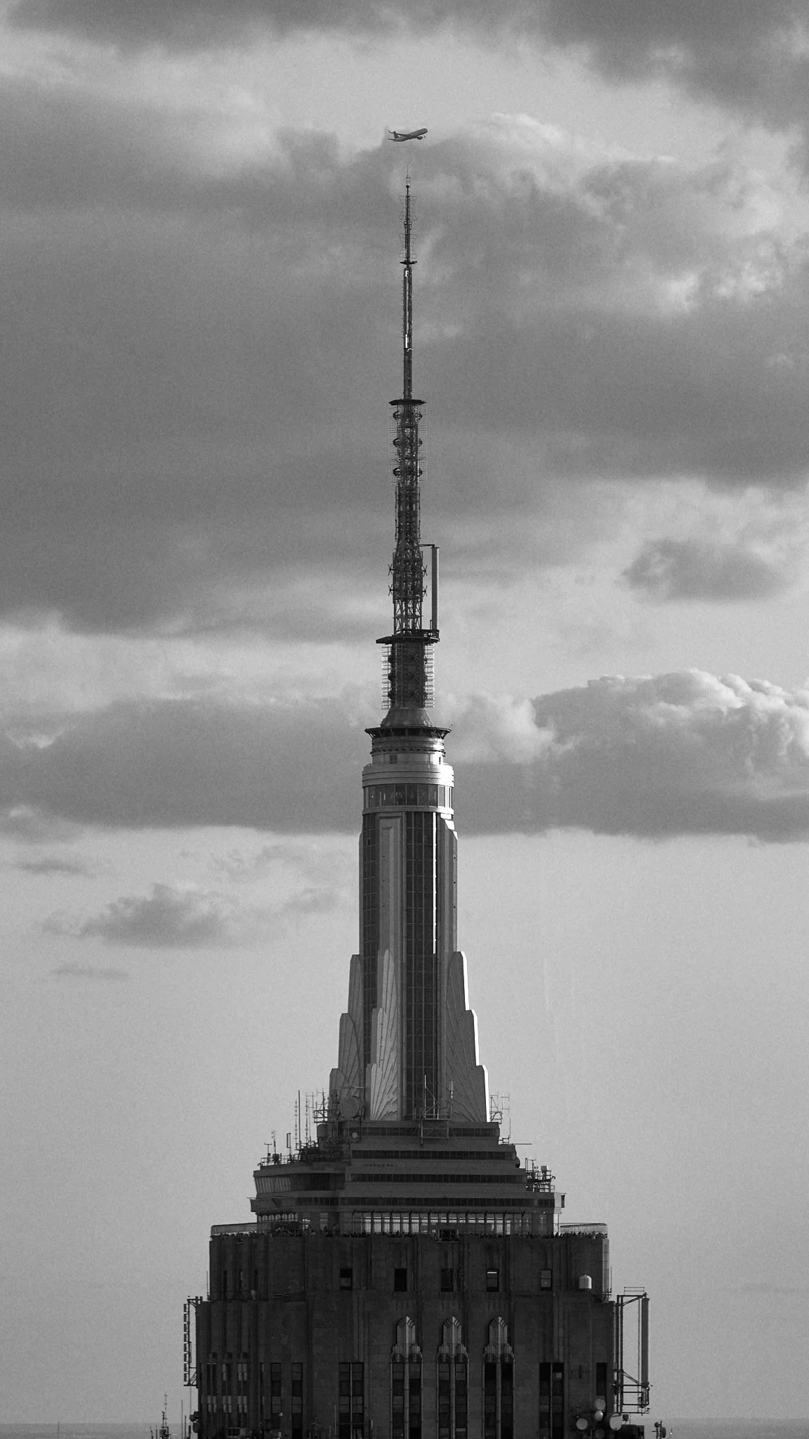 Black and white photo of the Empire State Building with an airplane flying above in the sky.