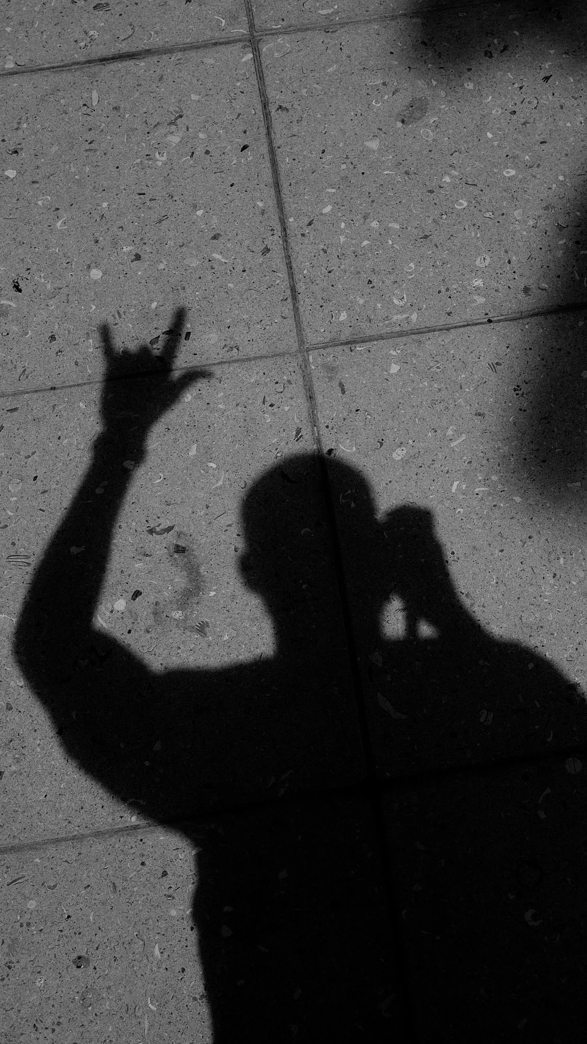 The shadow of a person on a tiled floor, making a hand gesture with their fingers.