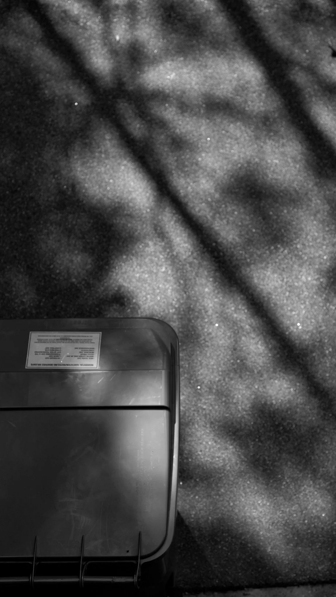 A partially visible metallic toaster sitting on a textured speckled surface with shadows cast across it.