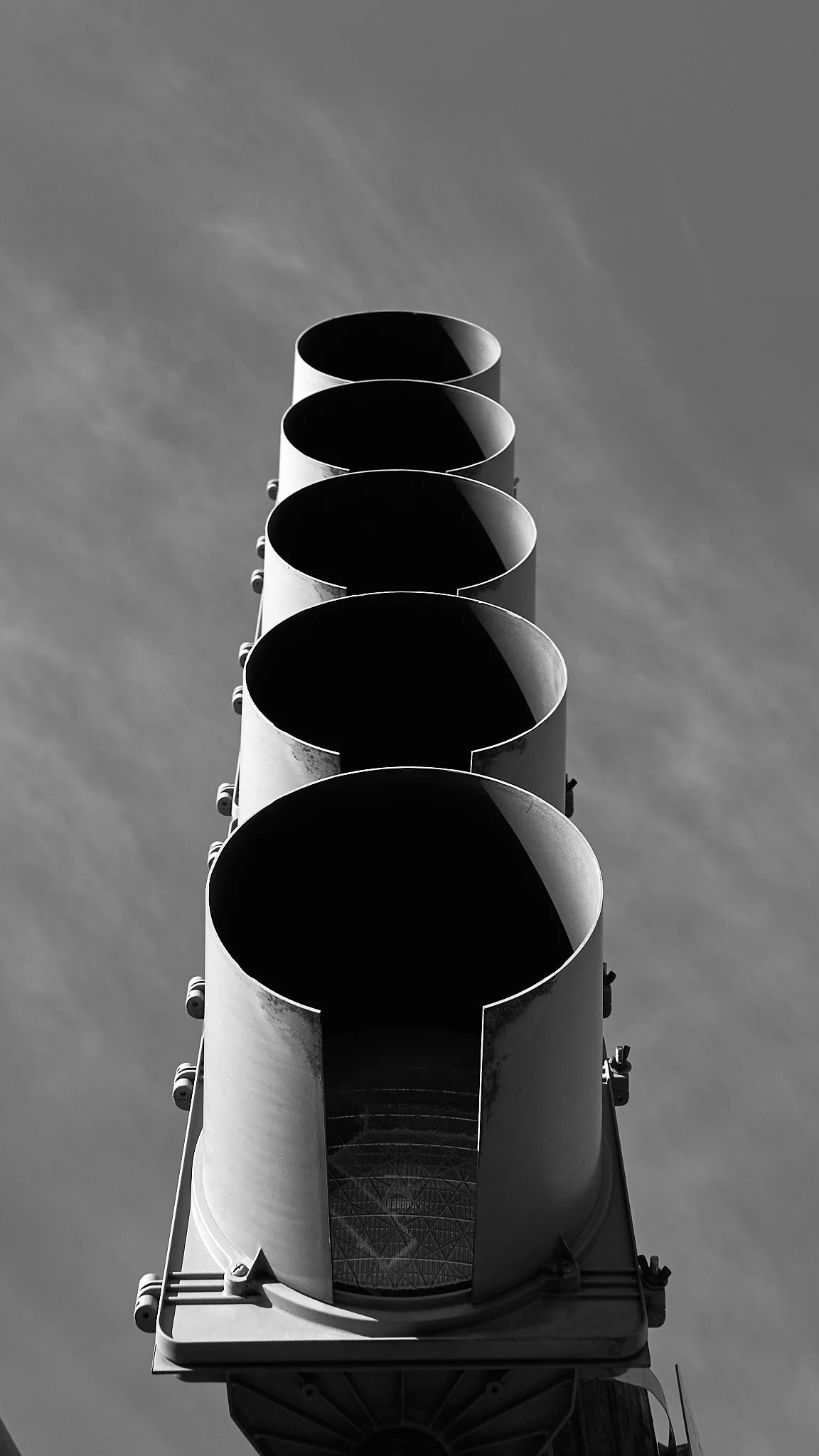 Black and white photo of a tall traffic light with five circular signals, viewed from below against a cloudy sky.