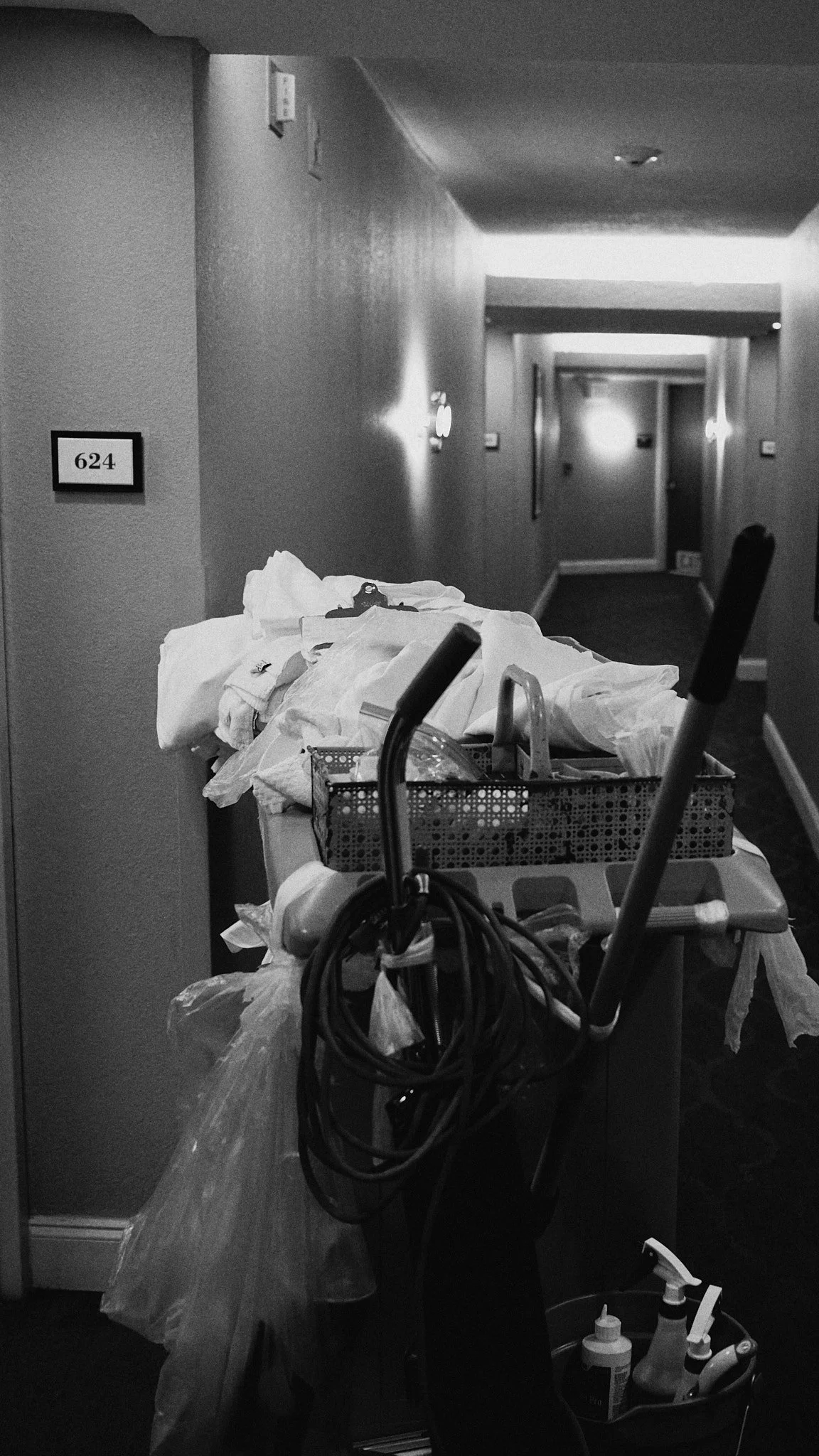 Cluttered hotel hallway with cleaning cart and supplies.