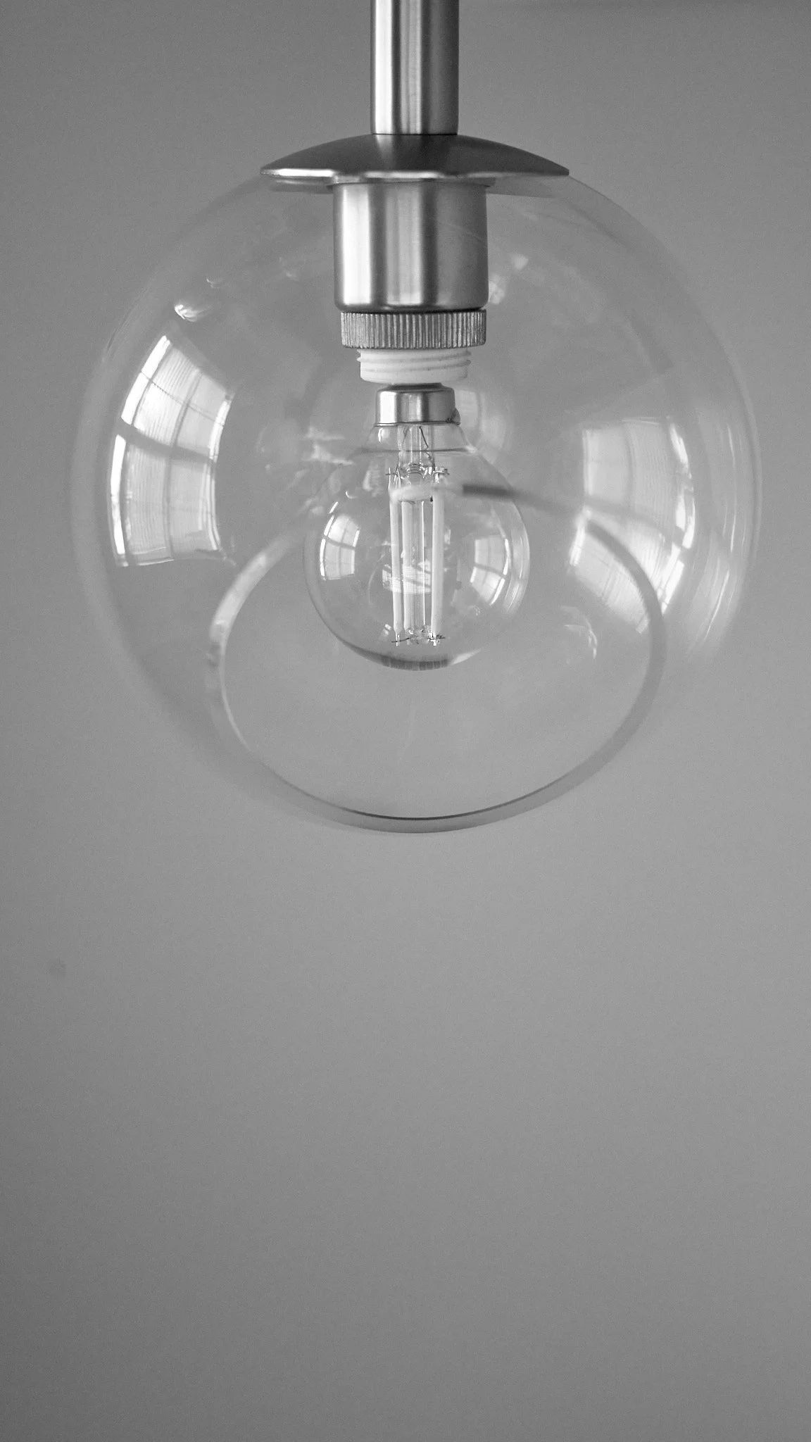 Close-up view of an illuminated incandescent light bulb hanging from a ceiling with a plain background.