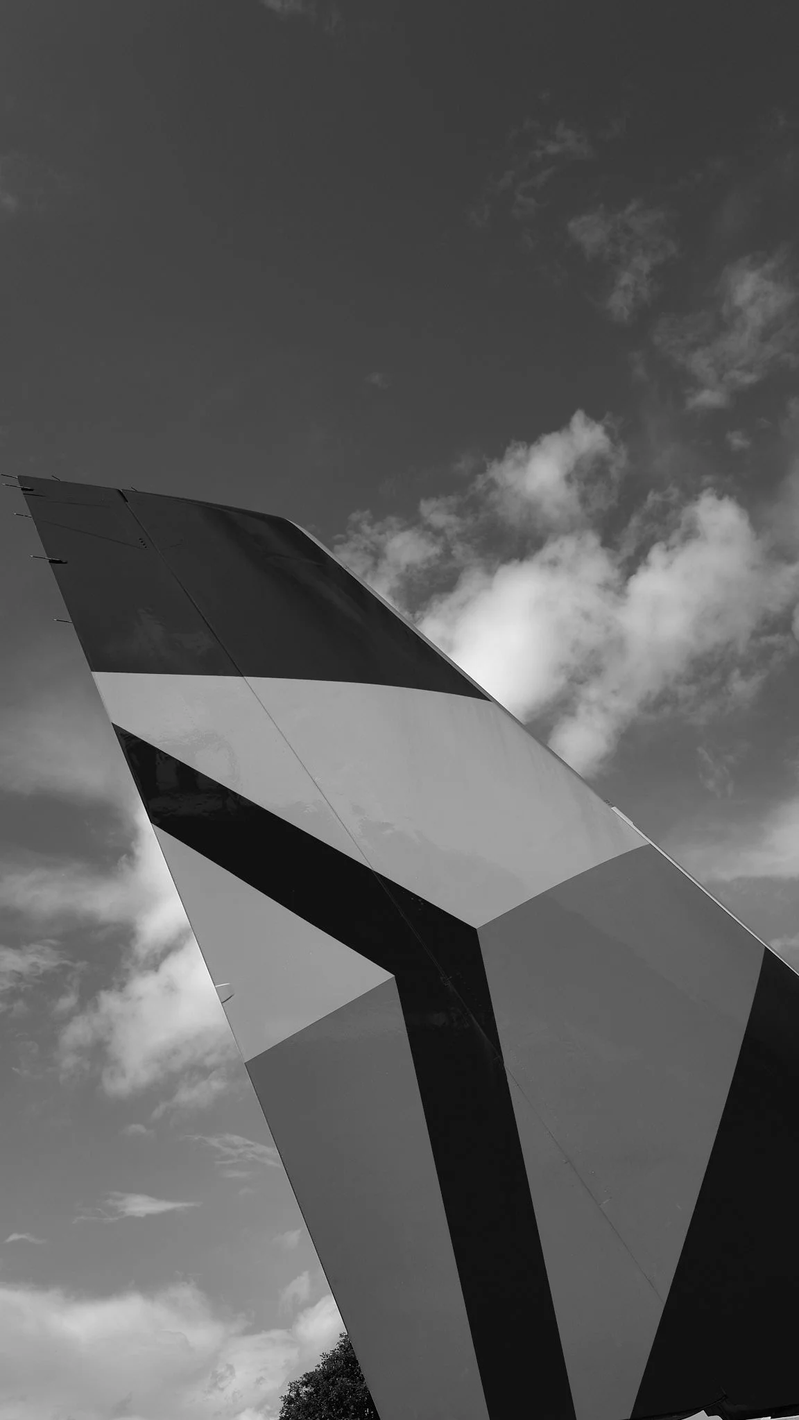 Close-up of an airplane tail with a geometric pattern, taken from a low angle against a partly cloudy sky.