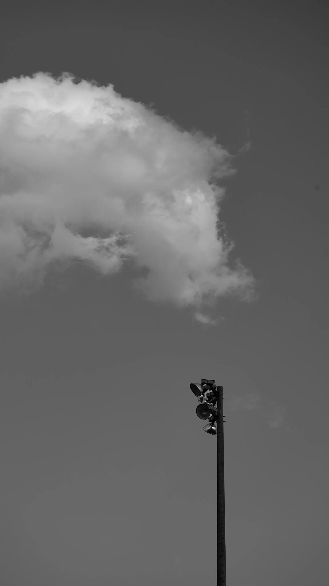 A tall stadium or floodlight pole with multiple lights attached, set against a sky with clouds.