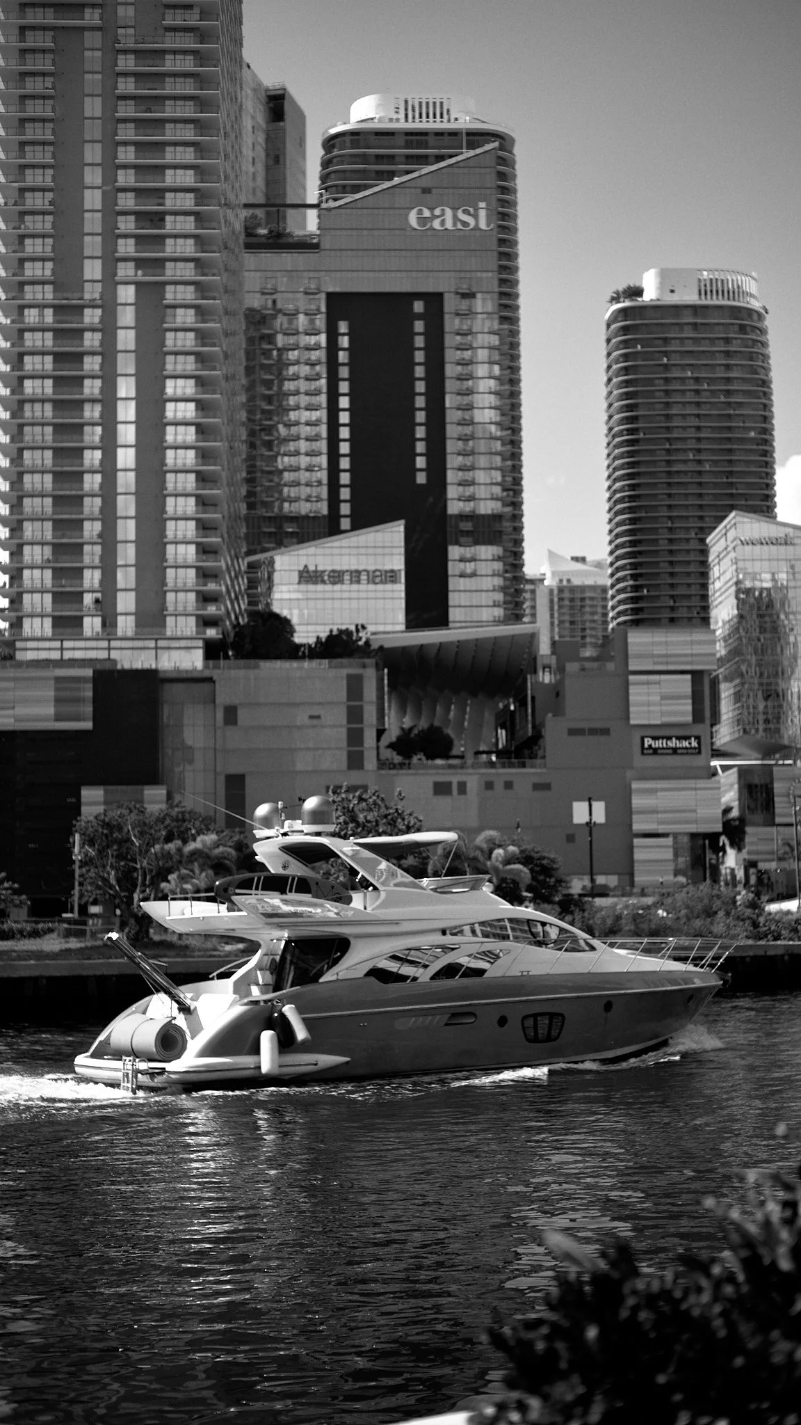 A luxury yacht sailing on a waterway with a backdrop of modern high-rise buildings in a city skyline.