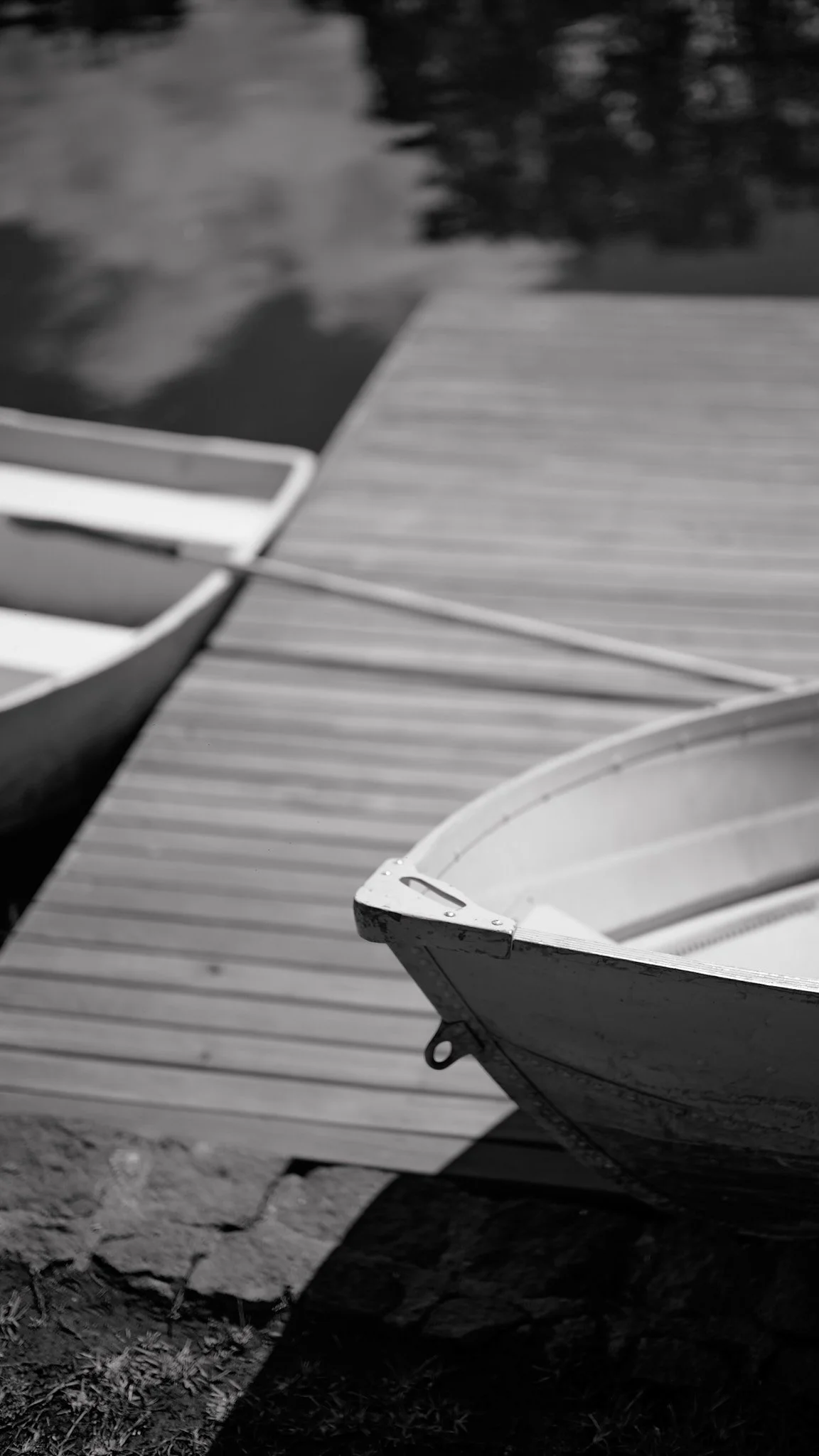 Black and white photo of boats docked at a wooden pier by a body of water.