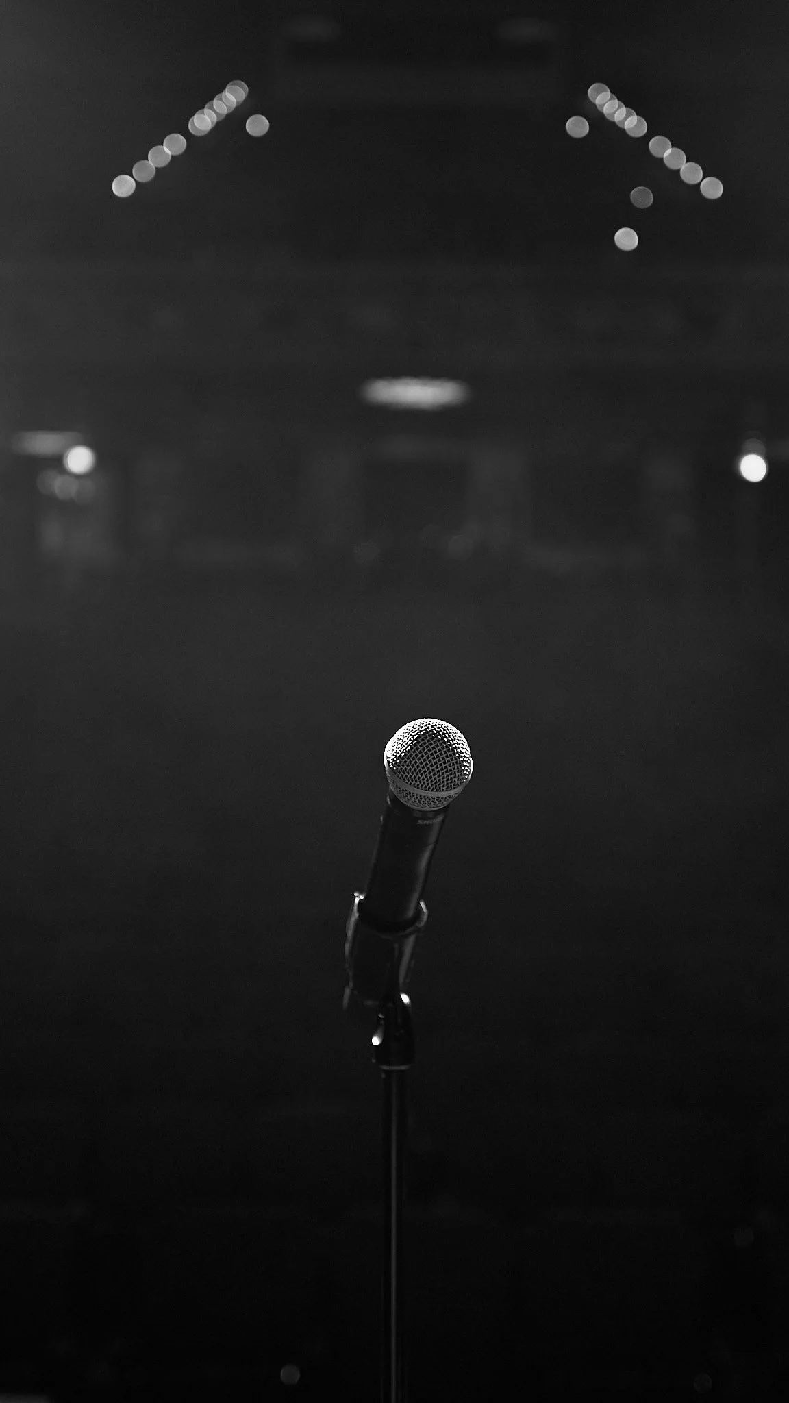 A microphone on a stage with a dark background, and blurred lights at the back.