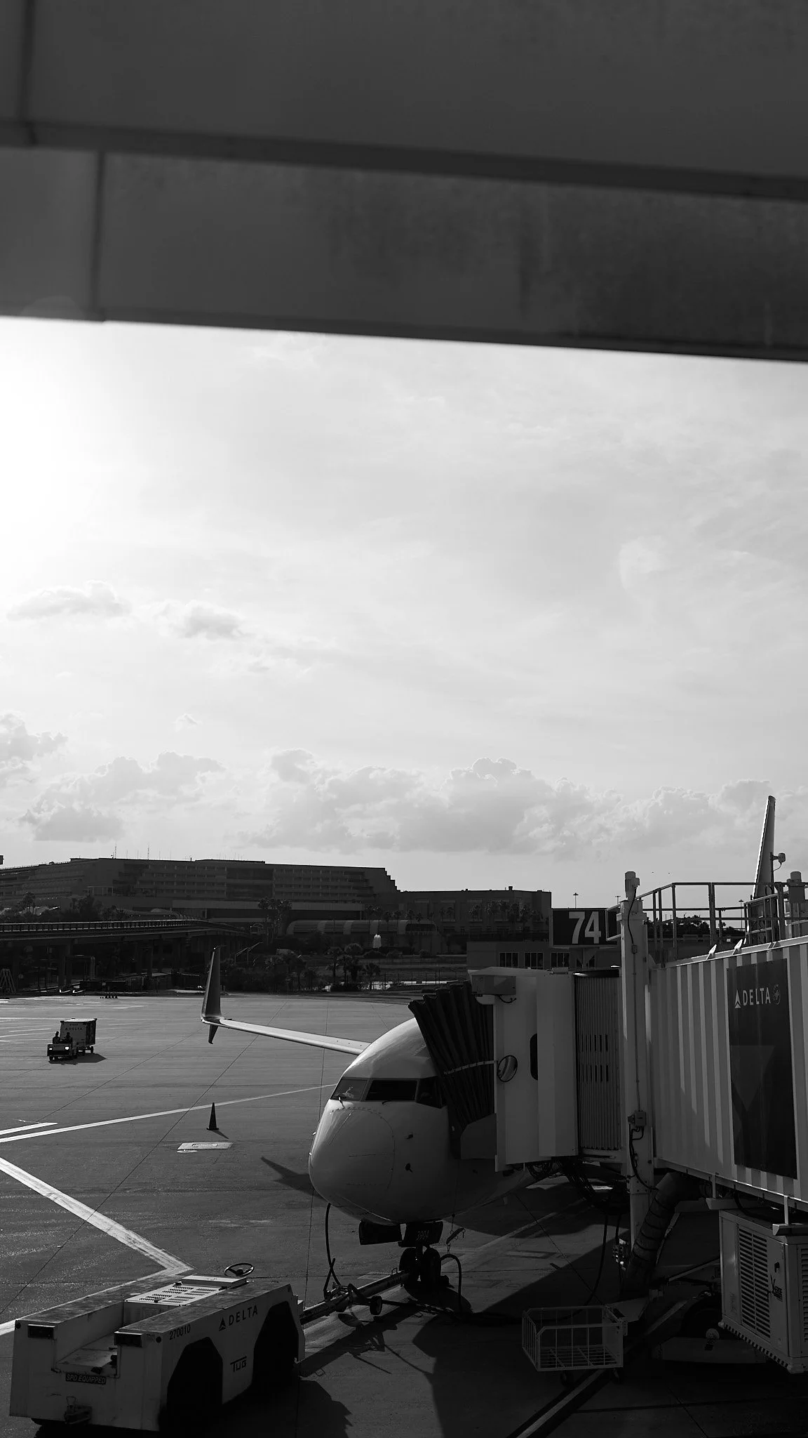 An airplane parked at a gate at an airport, connected to the terminal with a jet bridge, with a cloudy sky overhead.
