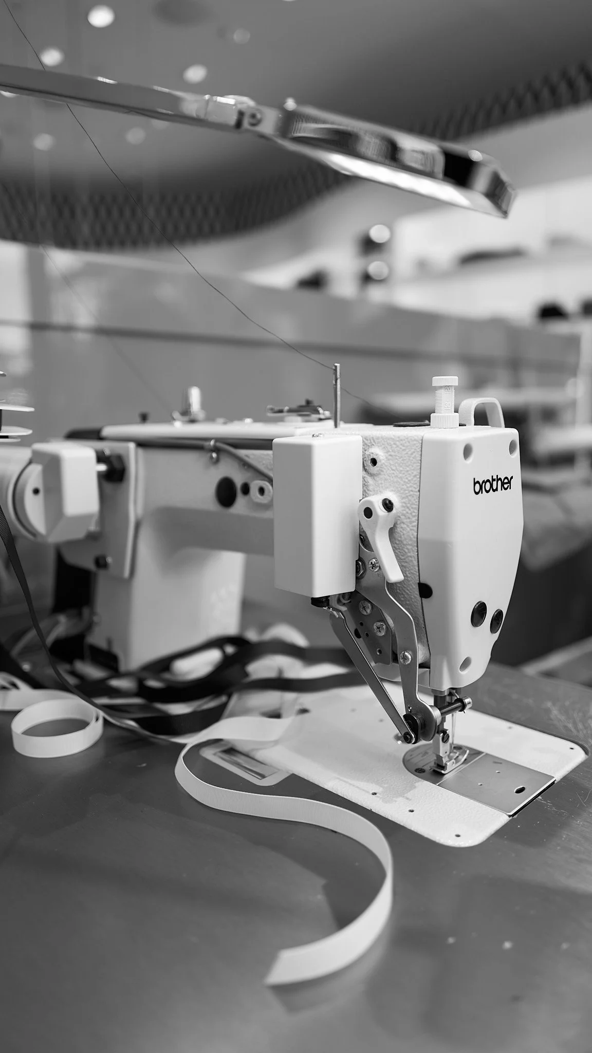 A sewing machine with the brand name 'Brother' in a workspace, with a strip of fabric or ribbon in front of it.