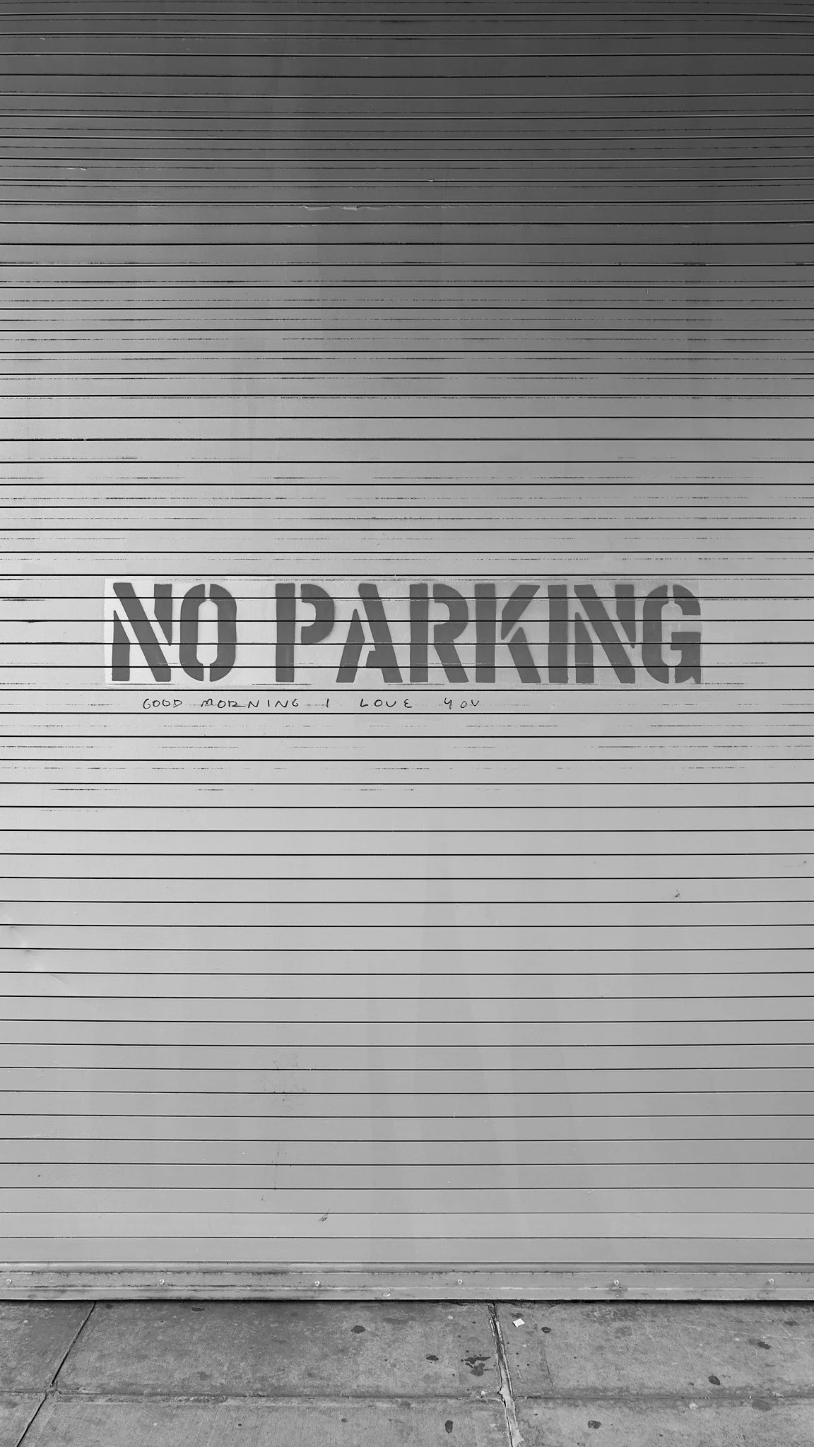 Closed metal garage door with a sign that says 'NO PARKING' and handwritten text underneath that reads 'Good morning-I love you'.