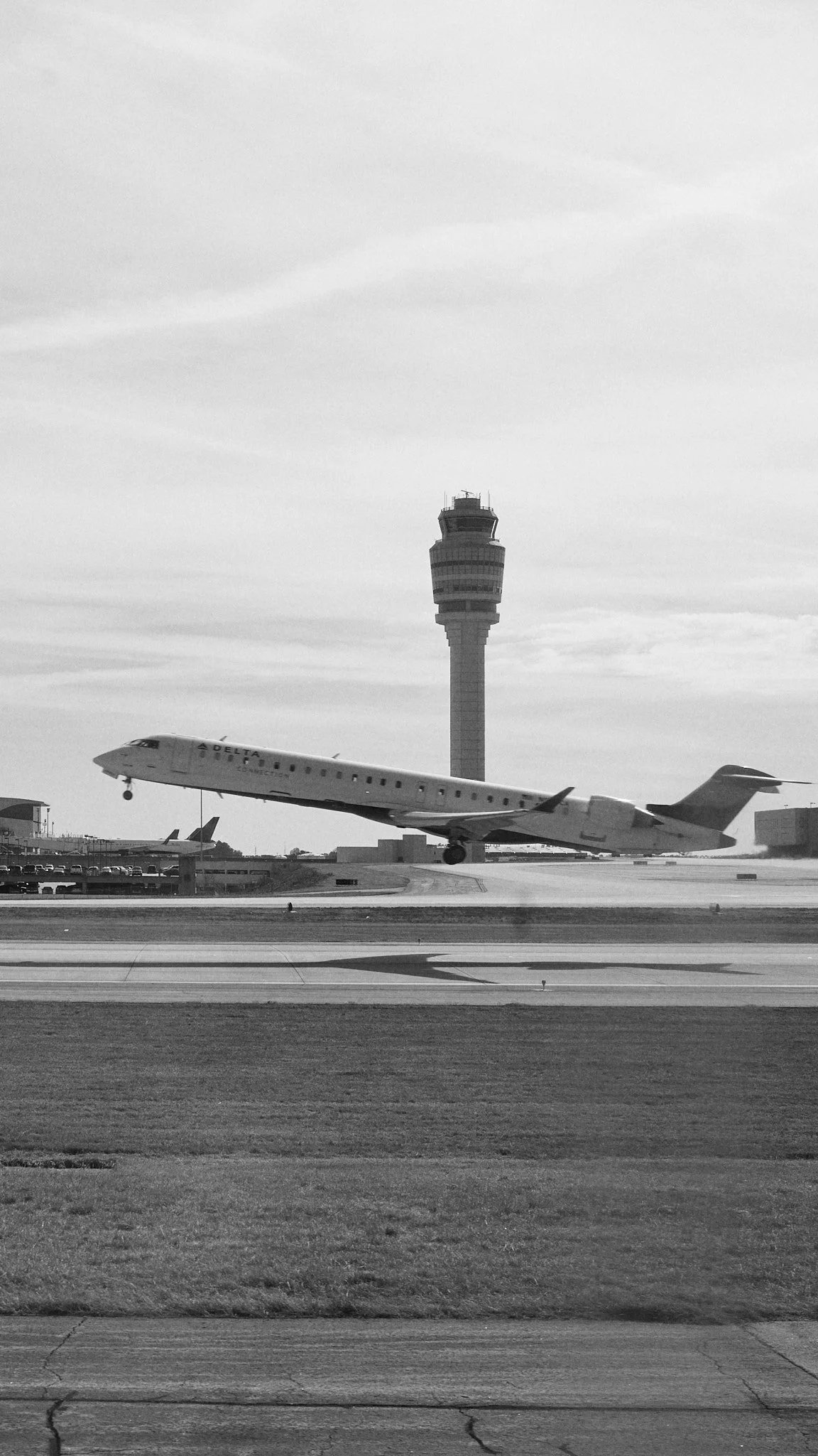 A Delta Airlines airplane taking off from an airport runway with an air traffic control tower in the background.