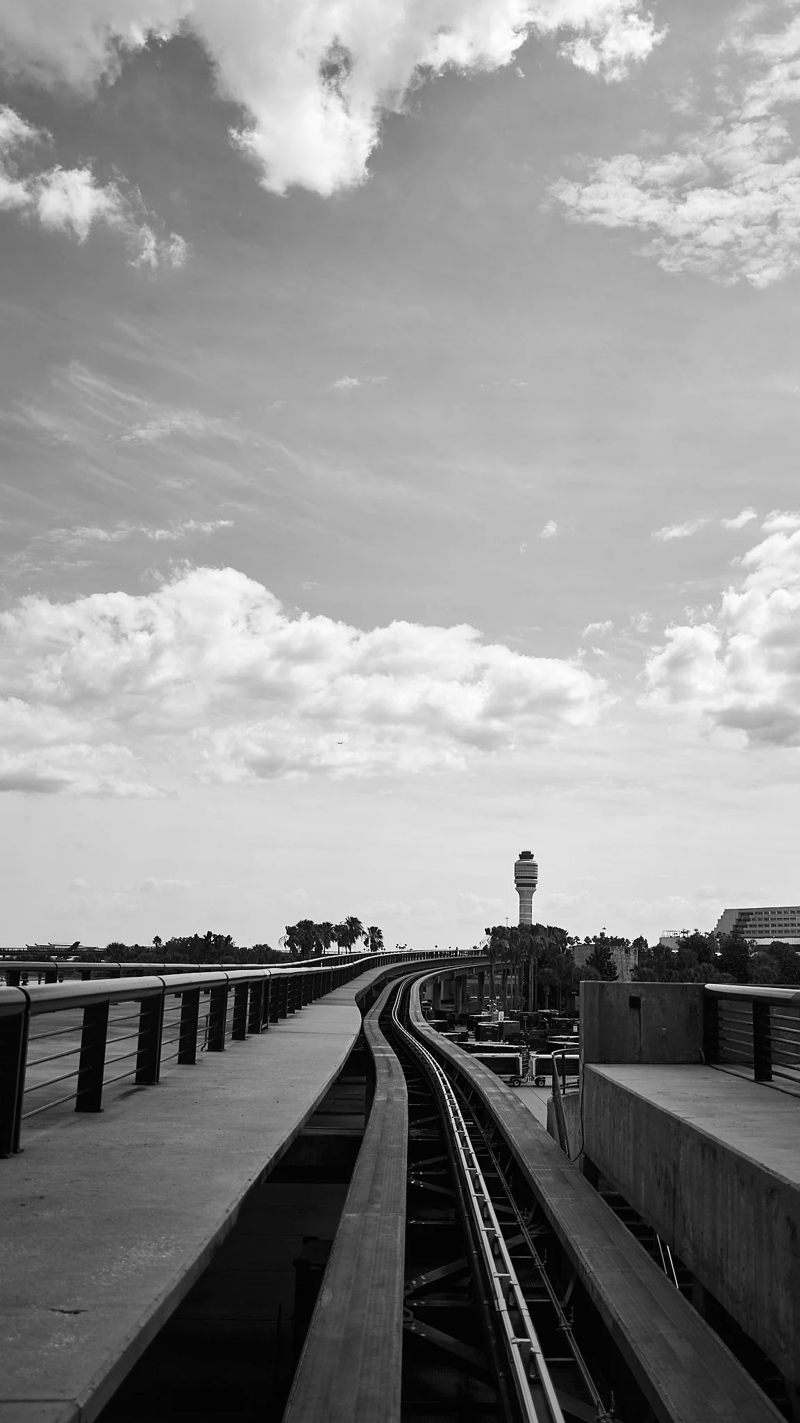 A black and white photo of an elevated railway track leading towards a cityscape with a tall observation tower in the background.