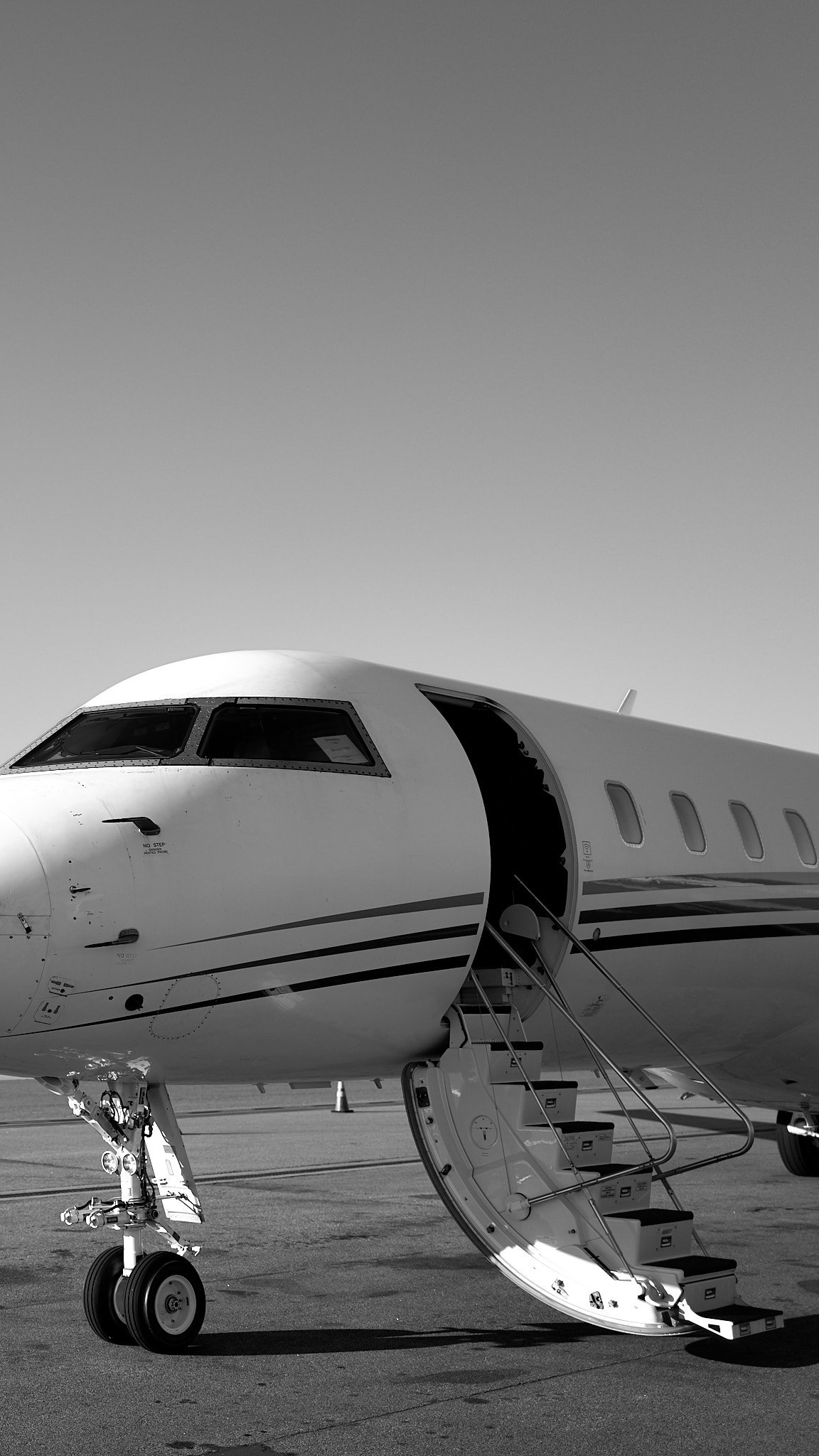 Black and white photo of private jet airplane with open entrance door and stairs on tarmac