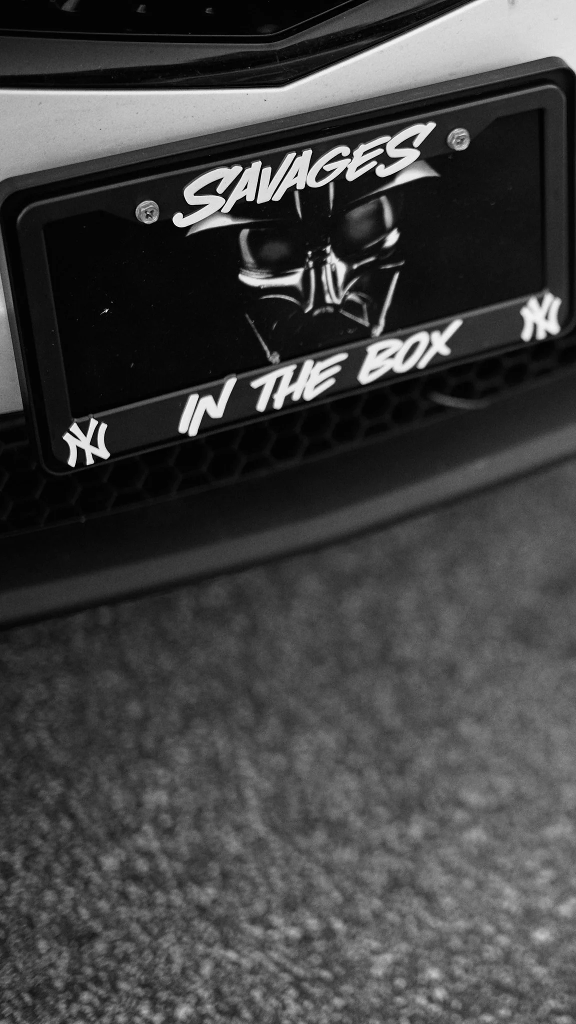 Close-up of a car's front grille with a custom black license plate reading 'SAVAGES IN THE BOX' and featuring the New York Yankees logo on each corner.
