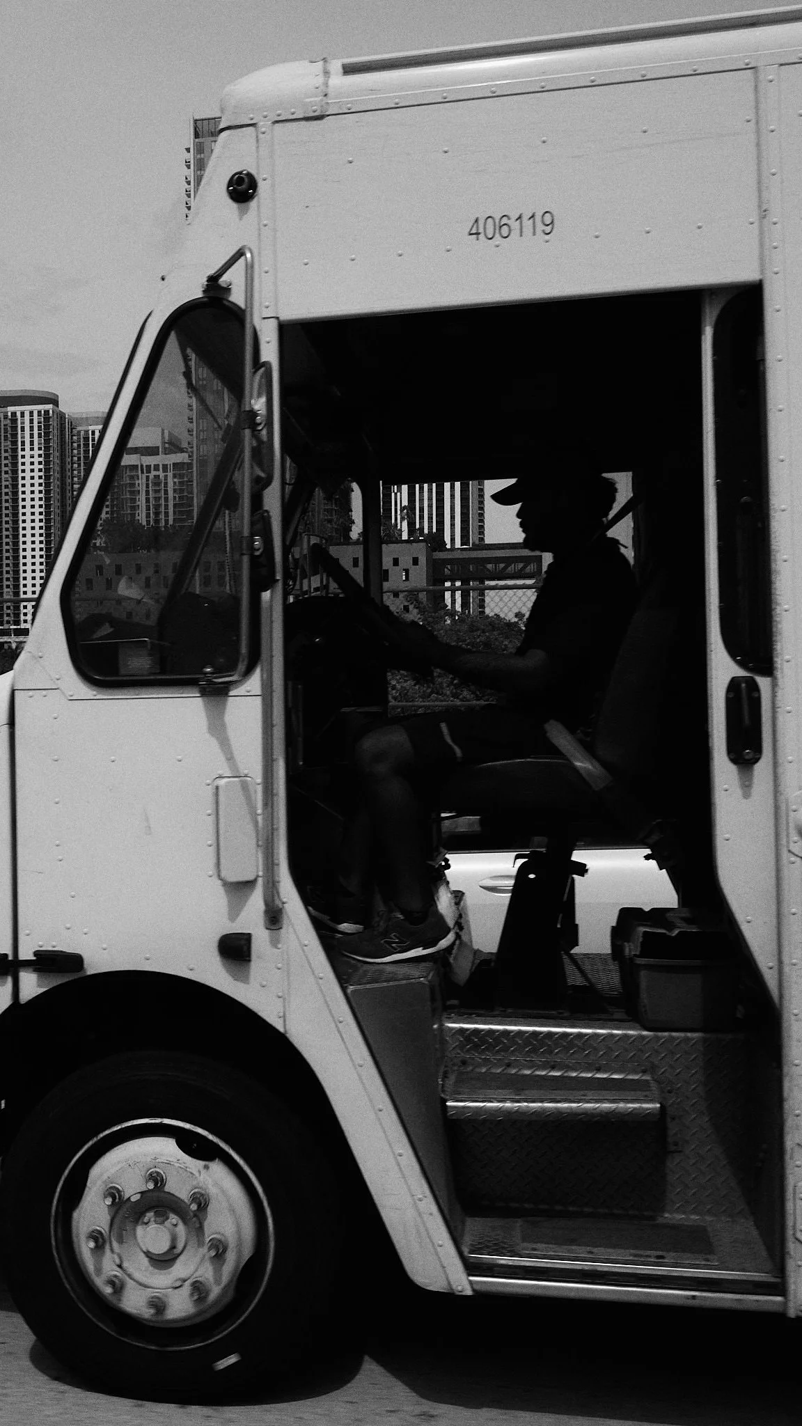 Silhouette of a person in a delivery truck interior, with city buildings visible in the background.