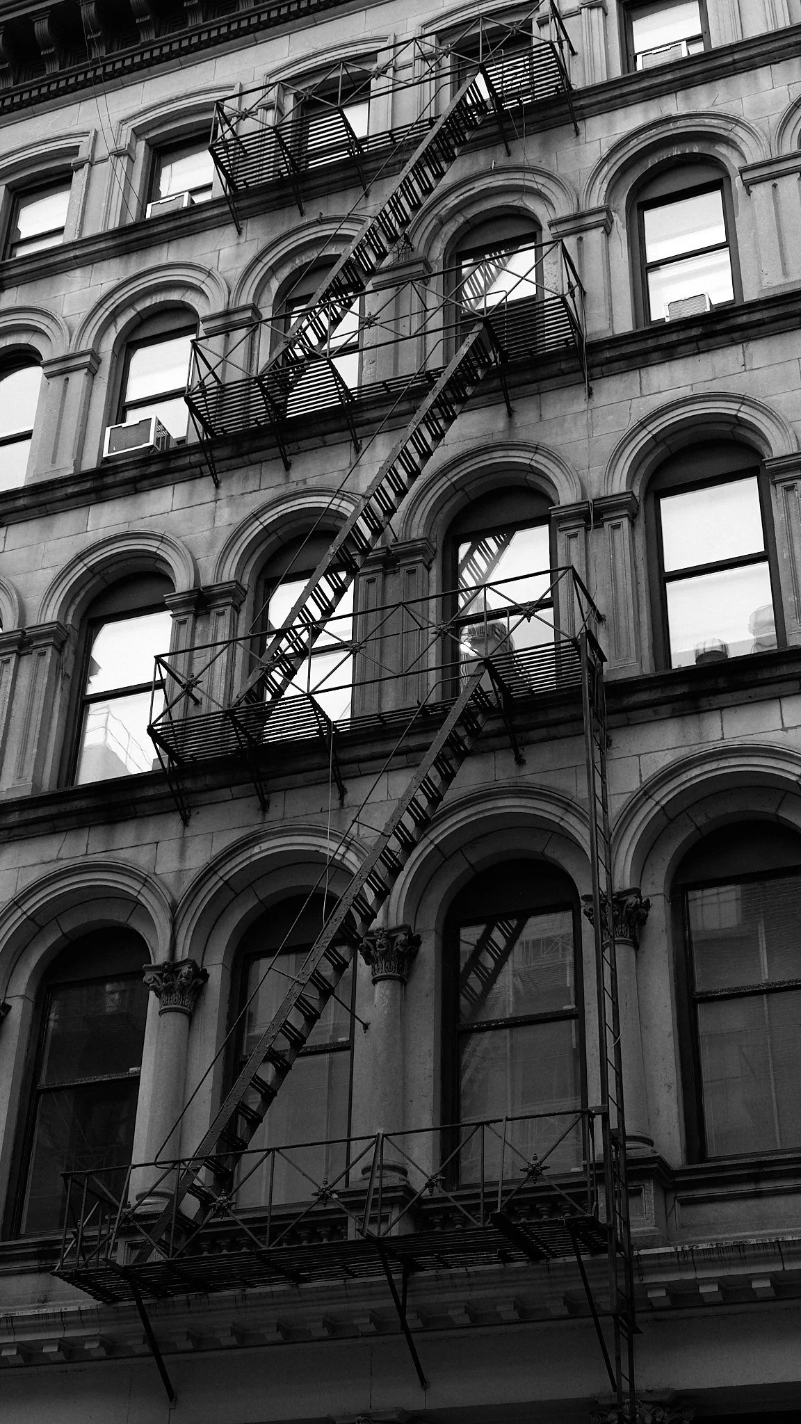 Black and white photo of a multi-story building with arched windows and fire escapes on the exterior.