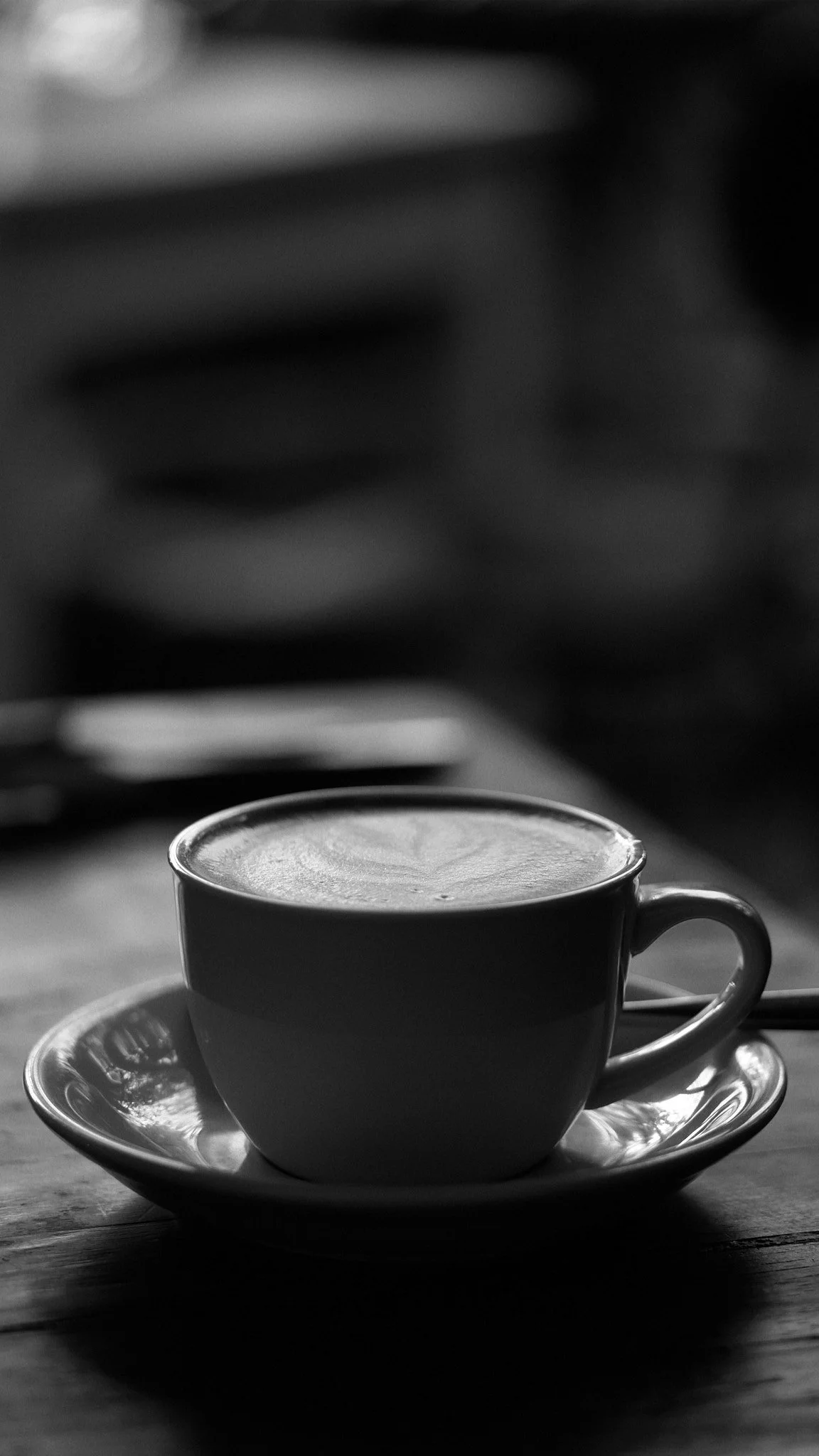 Black and white photo of a coffee cup on a saucer placed on a wooden table.