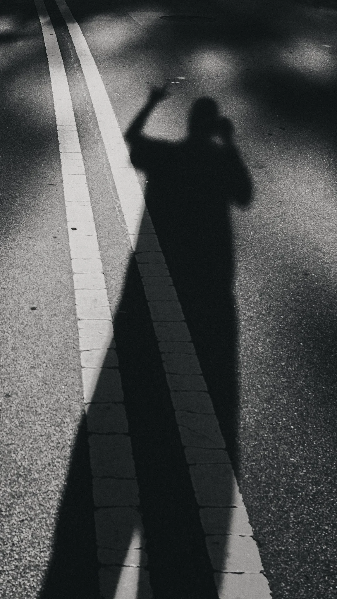 Shadow of a person taking a photo on a street at night, with a double solid white line and a brick pattern on the road.