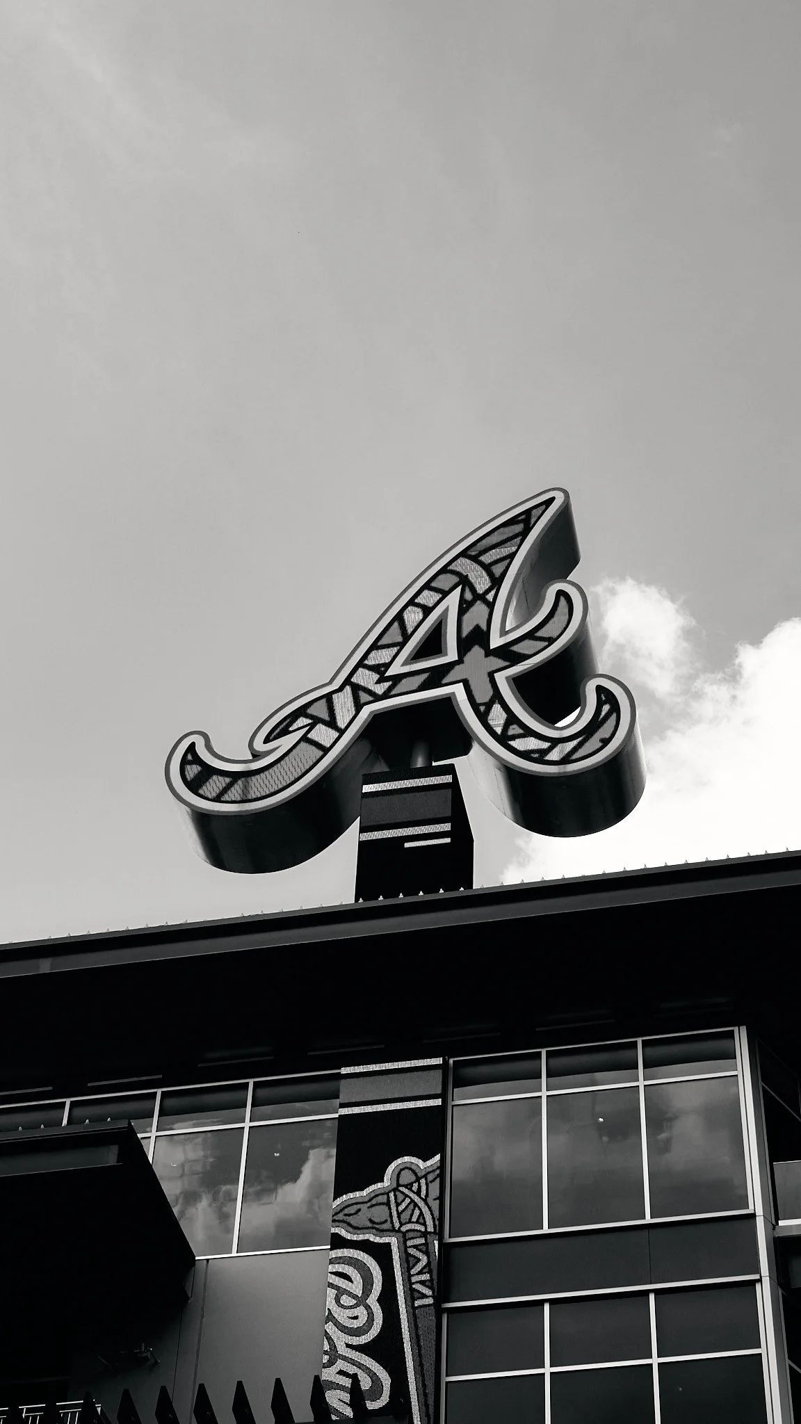 A black and white photo of a sign on top of a modern building with large glass windows, featuring a decorative letter 'A' with tribal or Celtic patterns.