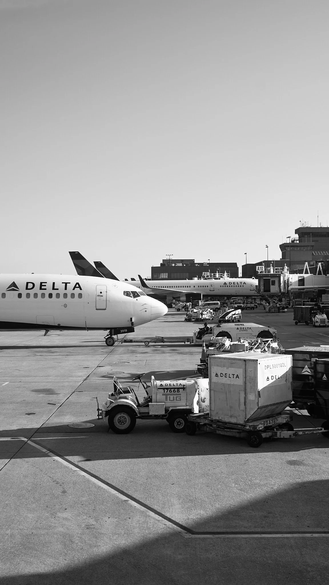 Black and white photo of an airport tarmac with Delta airplanes and ground service vehicles.