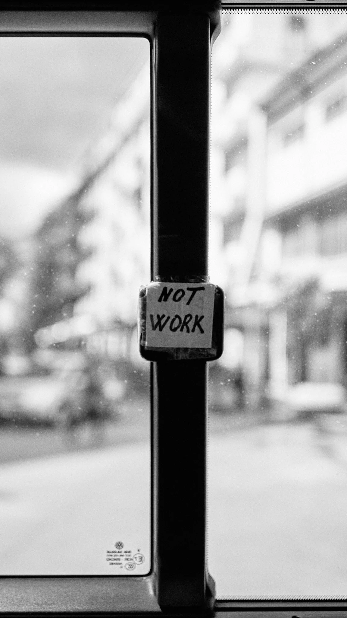View through bus window with a small sign on the door that says "NOT WORK" in handwritten letters.