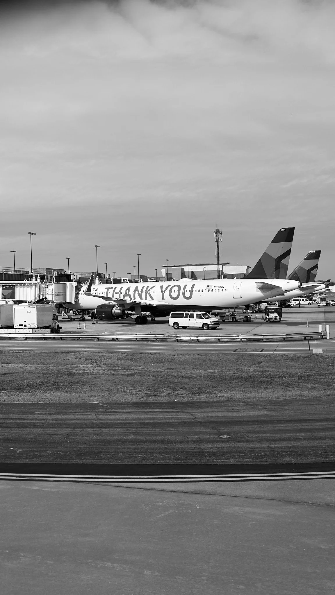 An airport tarmac with airplanes parked at gates, one with 'THANK YOU' written on its fuselage, under a partly cloudy sky.