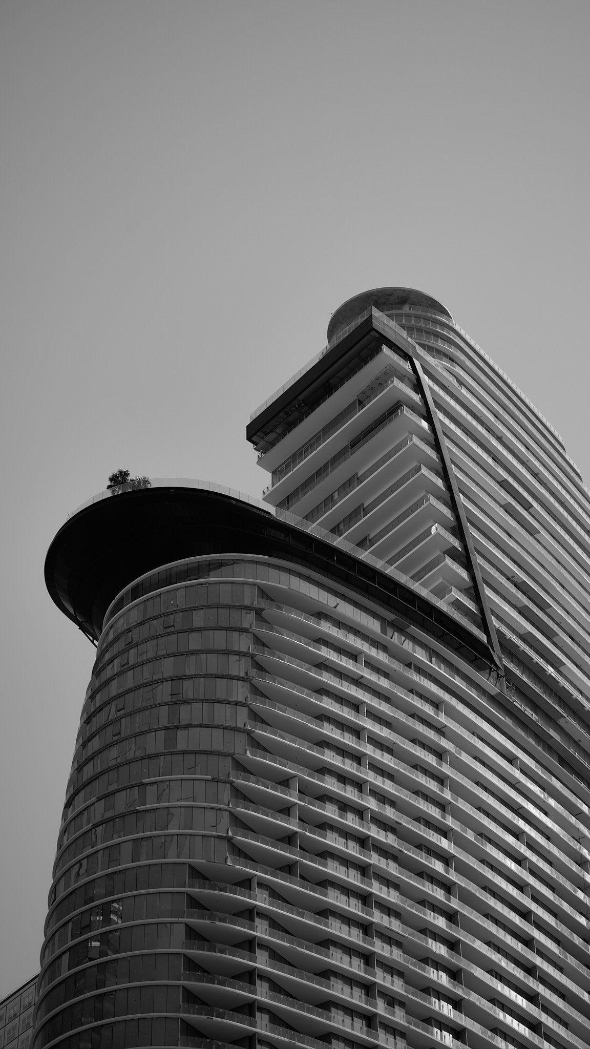 Black and white photo of a modern high-rise building with curved glass and multiple balconies, viewed from a low angle.