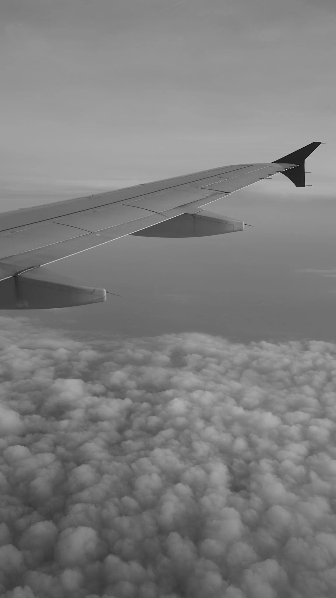 View of an airplane wing flying above the clouds in black and white.
