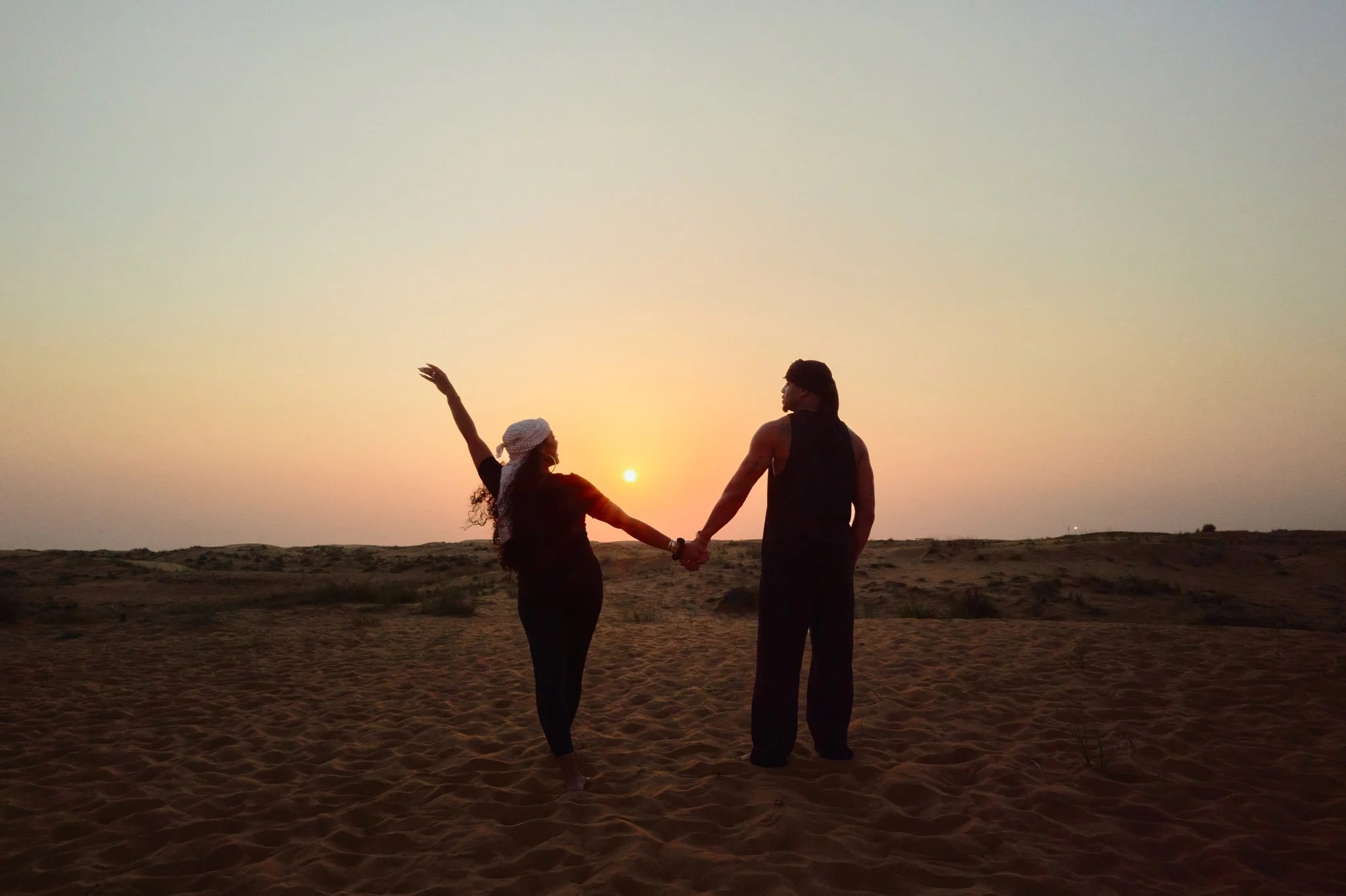Devale and Khadeen Ellis holding hands in desert at sunset, with one person raising the other hand.