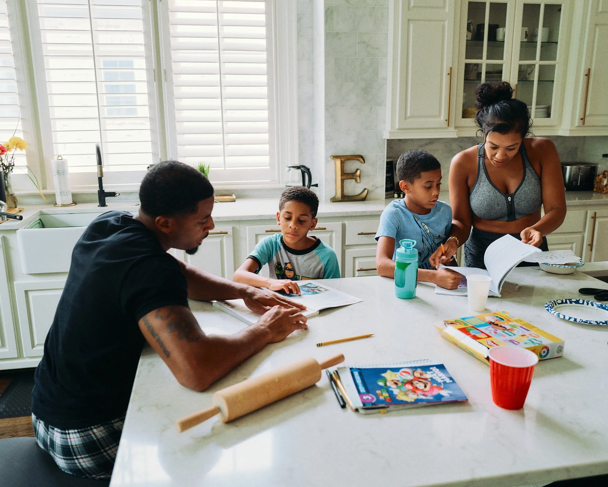 Family of five gathered around kitchen island doing homework and reading books together.