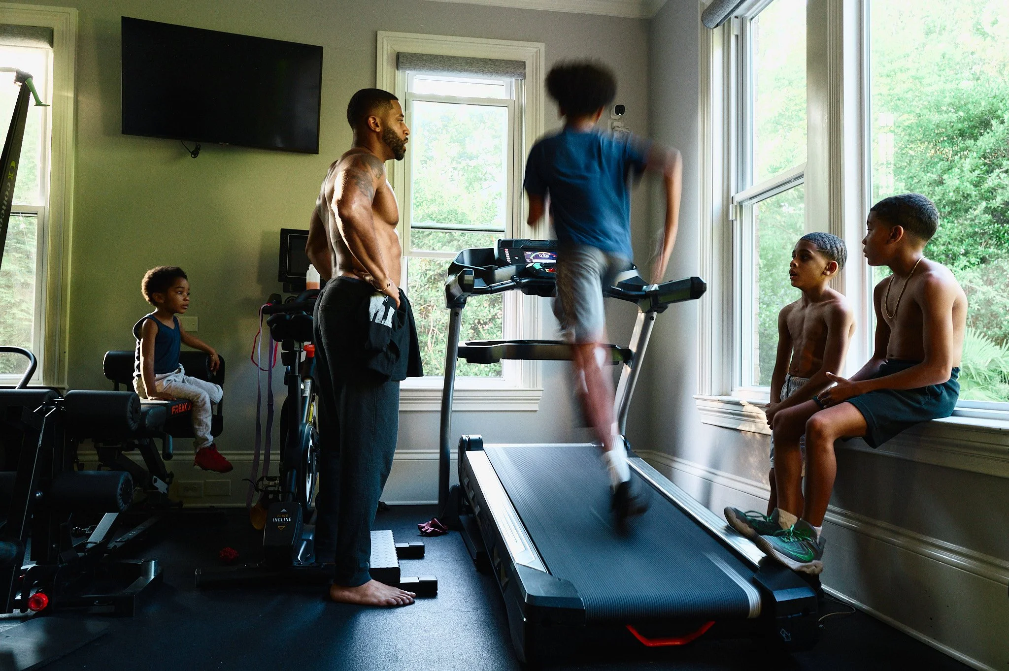 Devale Ellis and children in a home gym, with one child running on a treadmill and others watching.