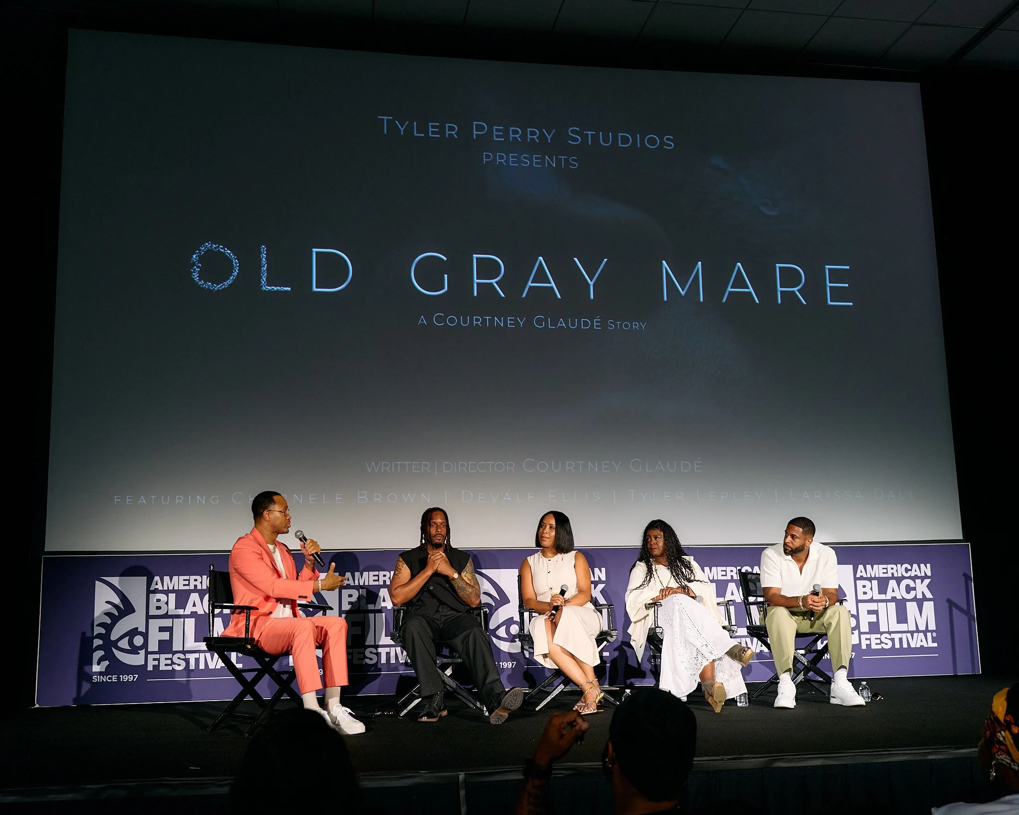 Panel discussion at the American Black Film Festival with five people seated on stage, in front of a large screen displaying the title 'Old Gray Mare' and credits for Courtney Glaudé, Devale Ellis and TPS surrounded by festival branding.