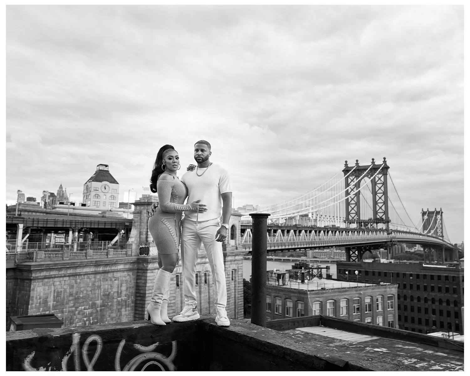 Khadeen and Devale Ellis stand together on a rooftop with the Brooklyn Bridge and Manhattan skyline in the background, black and white photograph.