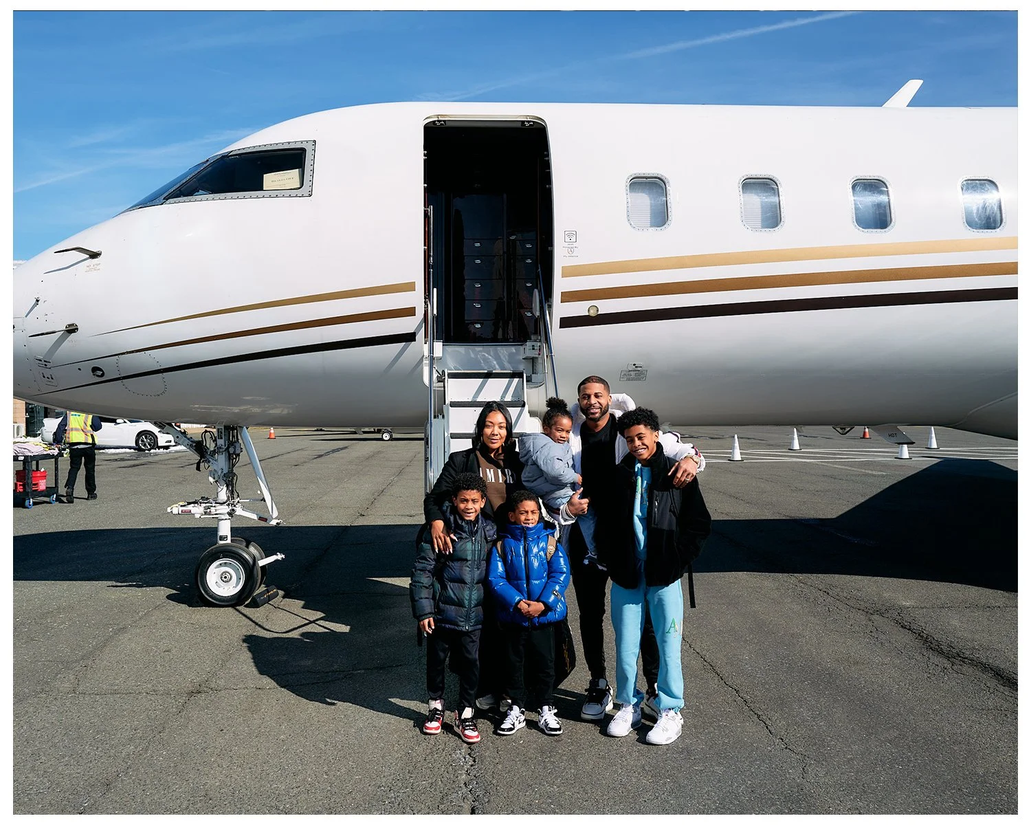 A family of six standing in front of a private jet on an airport tarmac, smiling and posing for a photo.