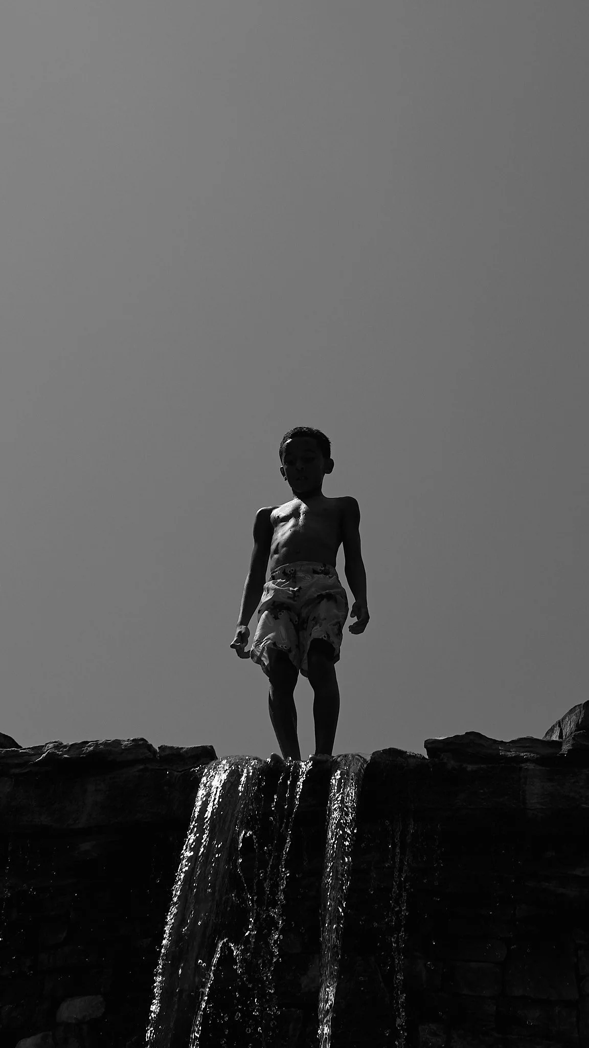 Kairo Ellis standing on a rocky ledge above a small waterfall, silhouetted against a clear sky.