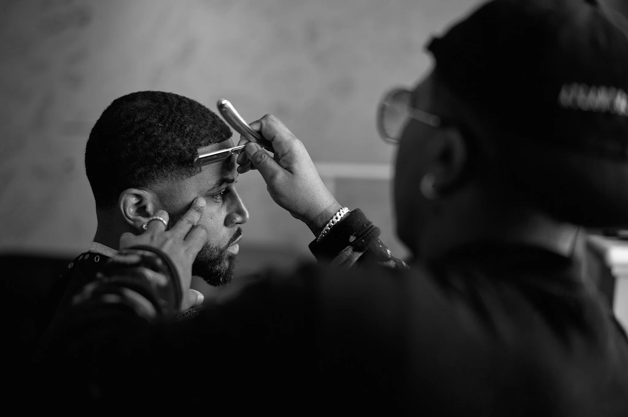 Tiff the barber giving Devale Ellis a haircut, focusing on trimming the man's hair with scissors and a razor.