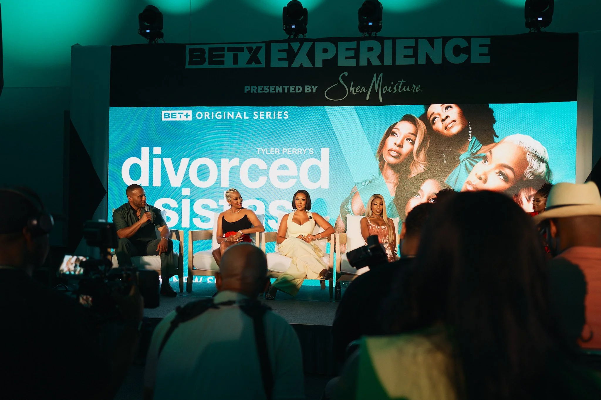 Panel discussion at BETX Experience for Tyler Perry's series 'Divorced Sisters,' with five people on stage and a large screen behind displaying promotional artwork and cast photos.