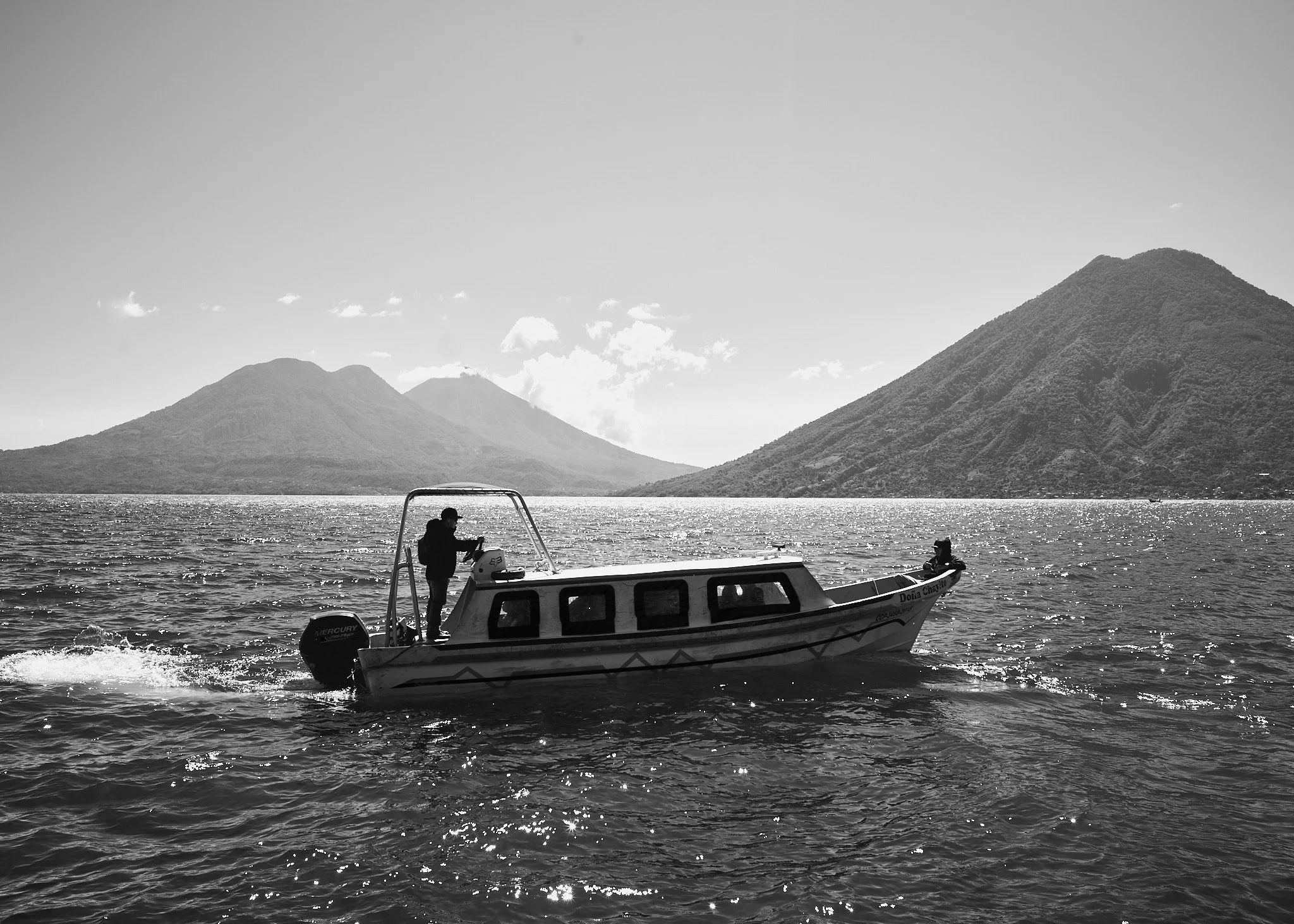 A boat on a lake with mountains in the background, black and white photo.
