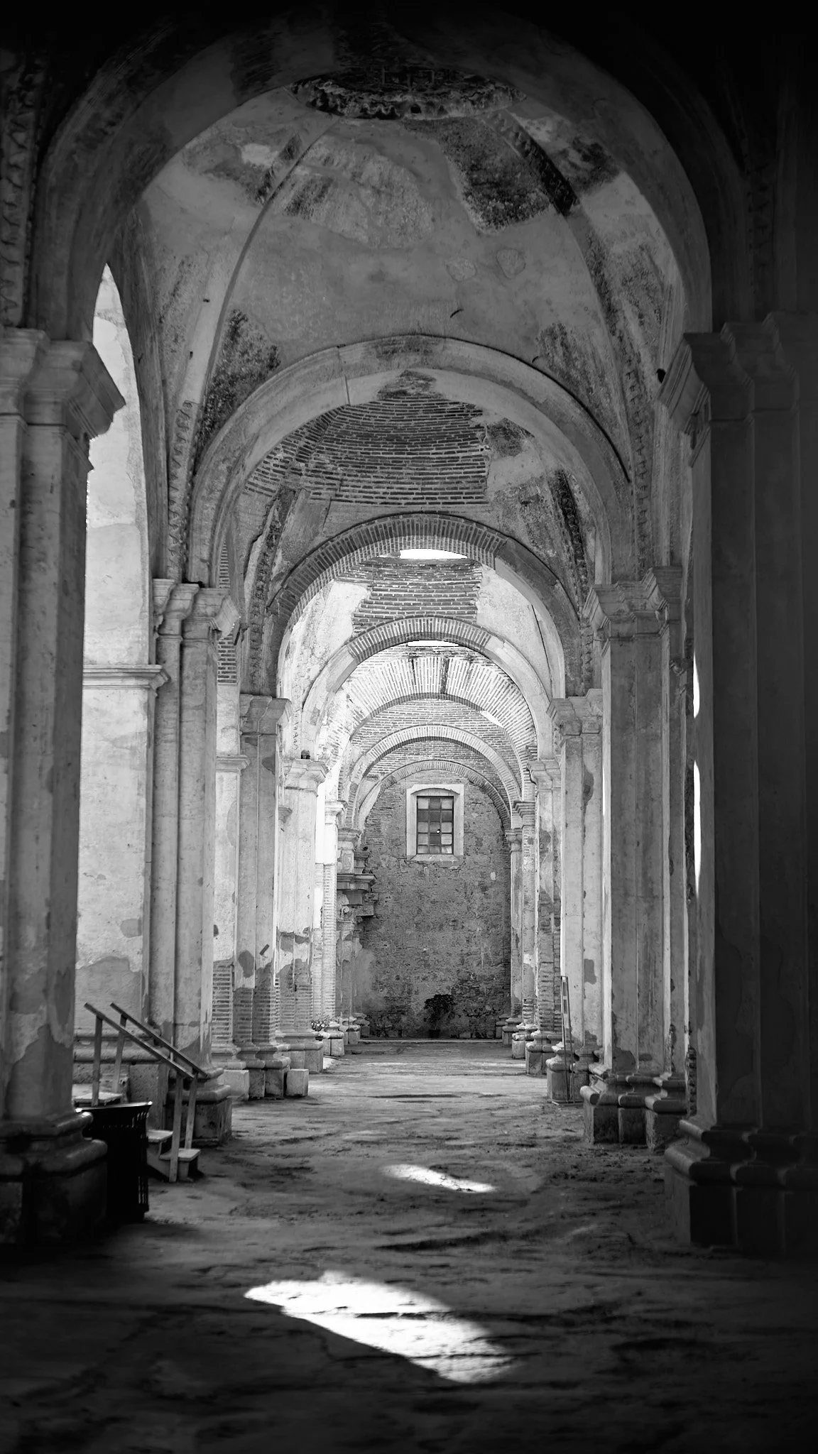 Black and white photograph of an old church or cathedral interior with high arches, columns, and a weathered floor.