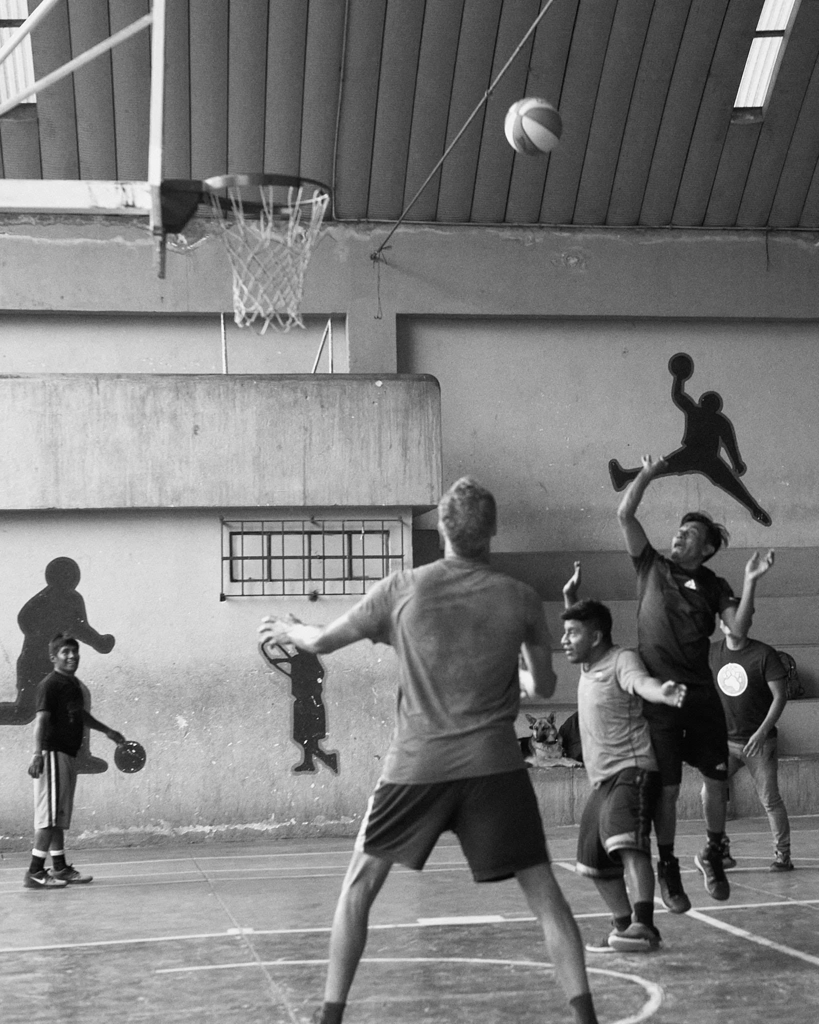People playing basketball in an indoor gym with wall decorations of silhouetted basketball players.