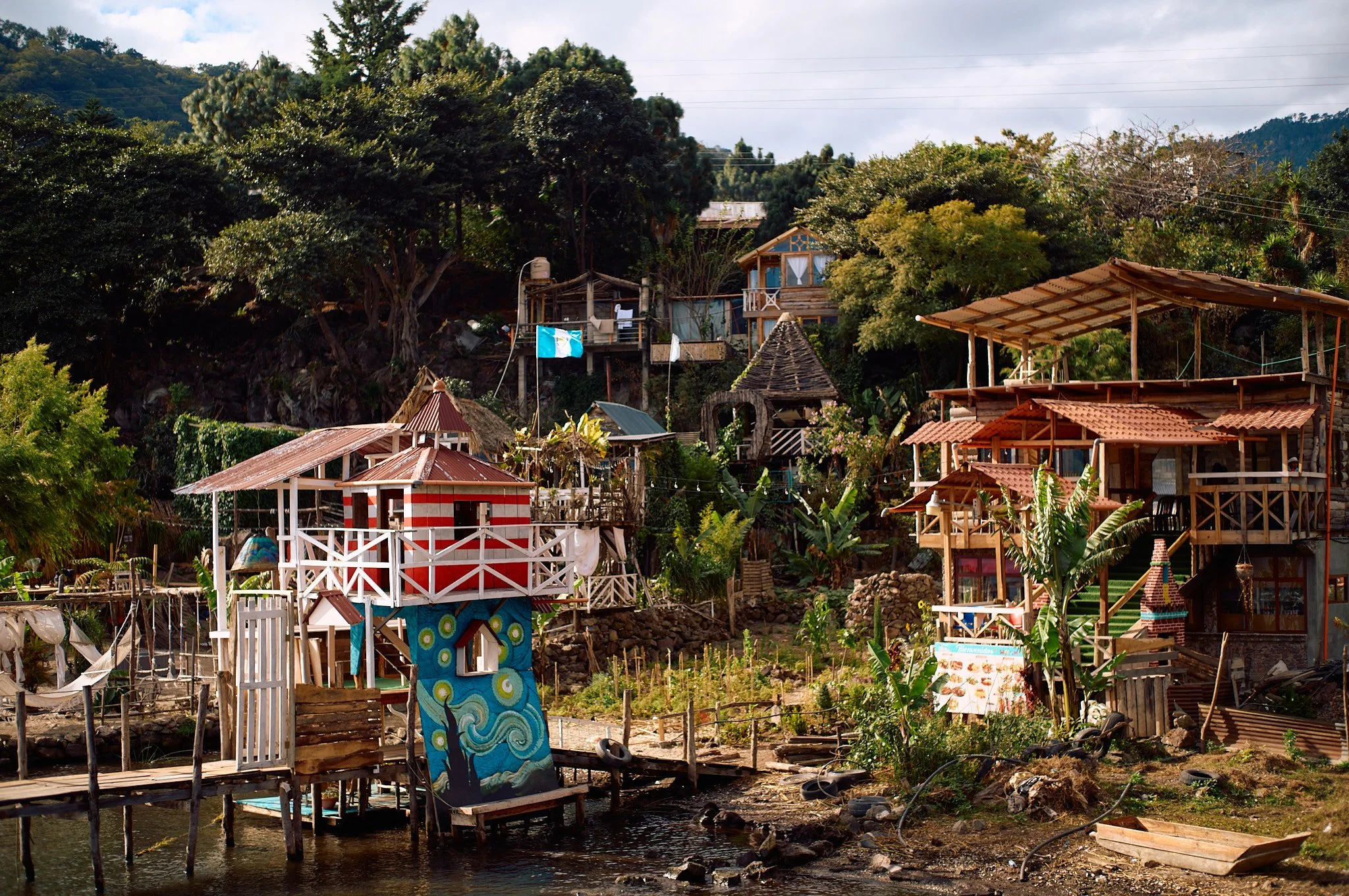 Colorful houses on a hillside near water with lush greenery and trees in the background.